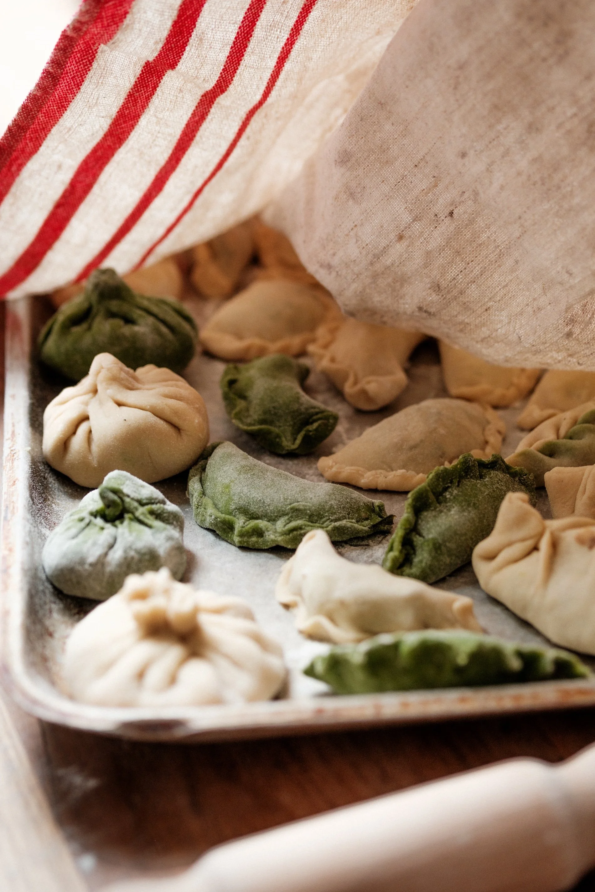 A tray of dumplings can be seen under a white cloth, ready to be cooked