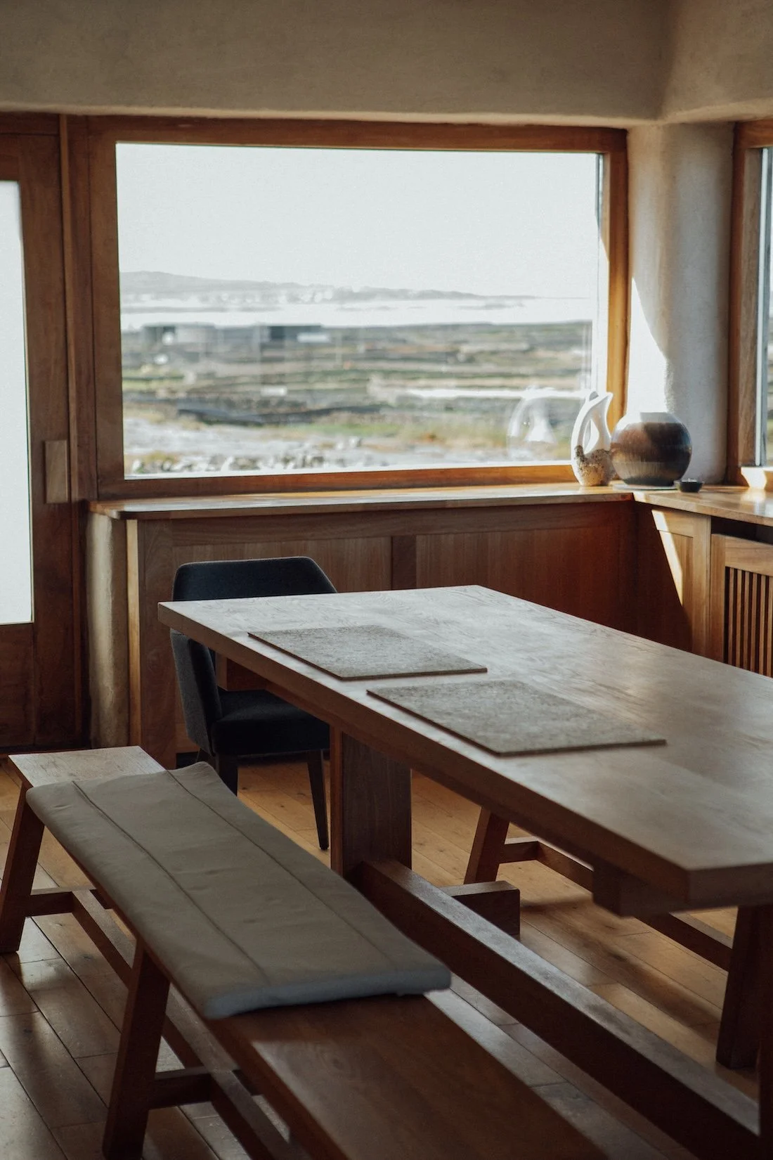 A hand-carved wooden table is illuminated by sunlight coming through a huge window overlooking the rocky Irish coast.