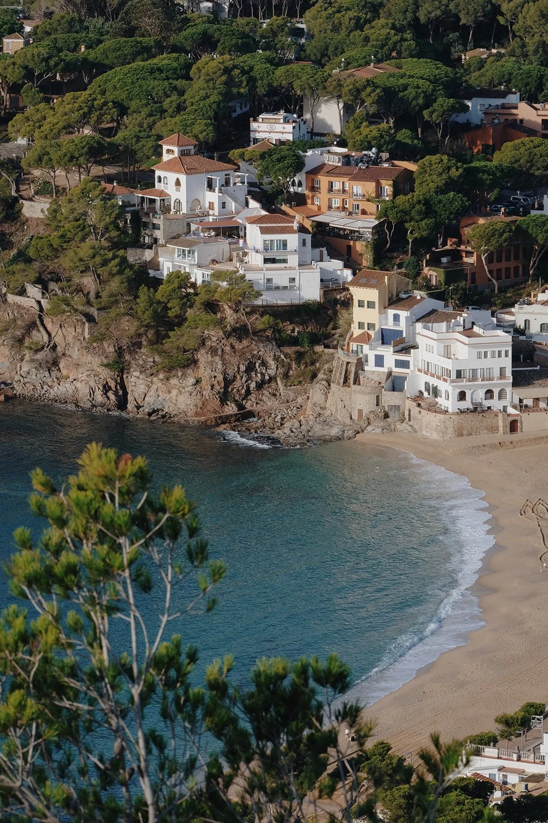 whitewashed buildings surrounded by native trees overlook a quiet cove in Spain's Costa Brava