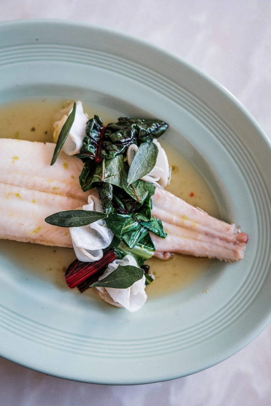A close up of poached trout topped with green foraged vegetables