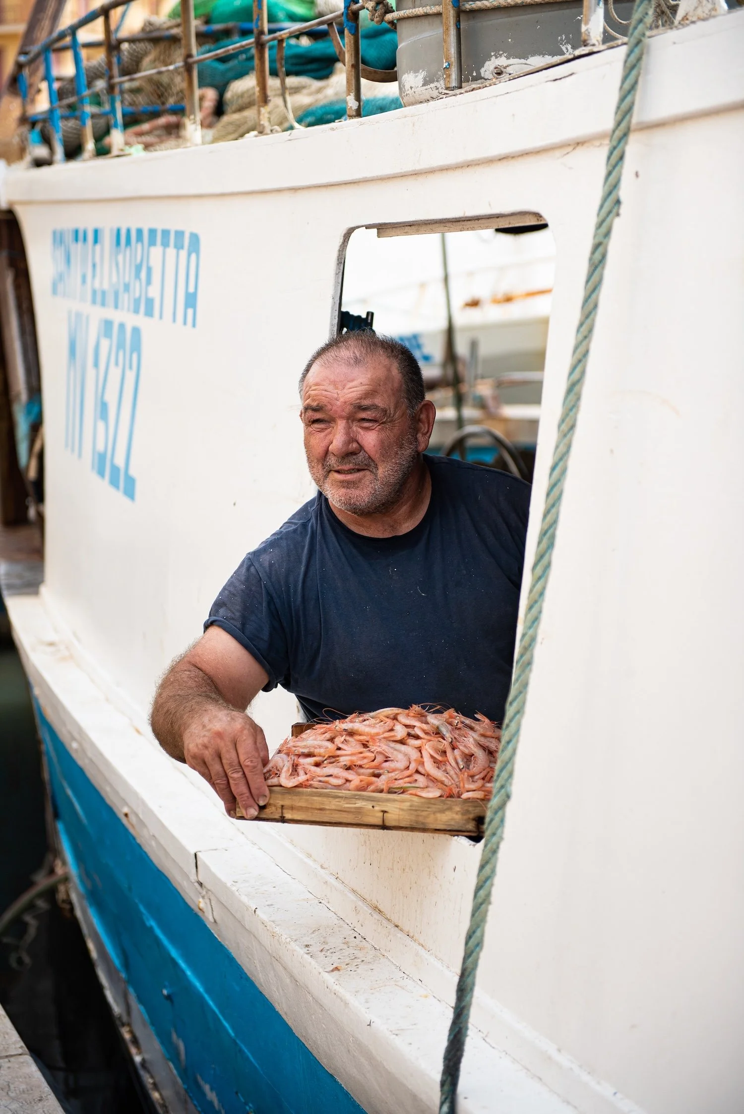 A fisherman leans out the window of his white and blue boat with a tray of freshly-caught gambero rosso (prawns)