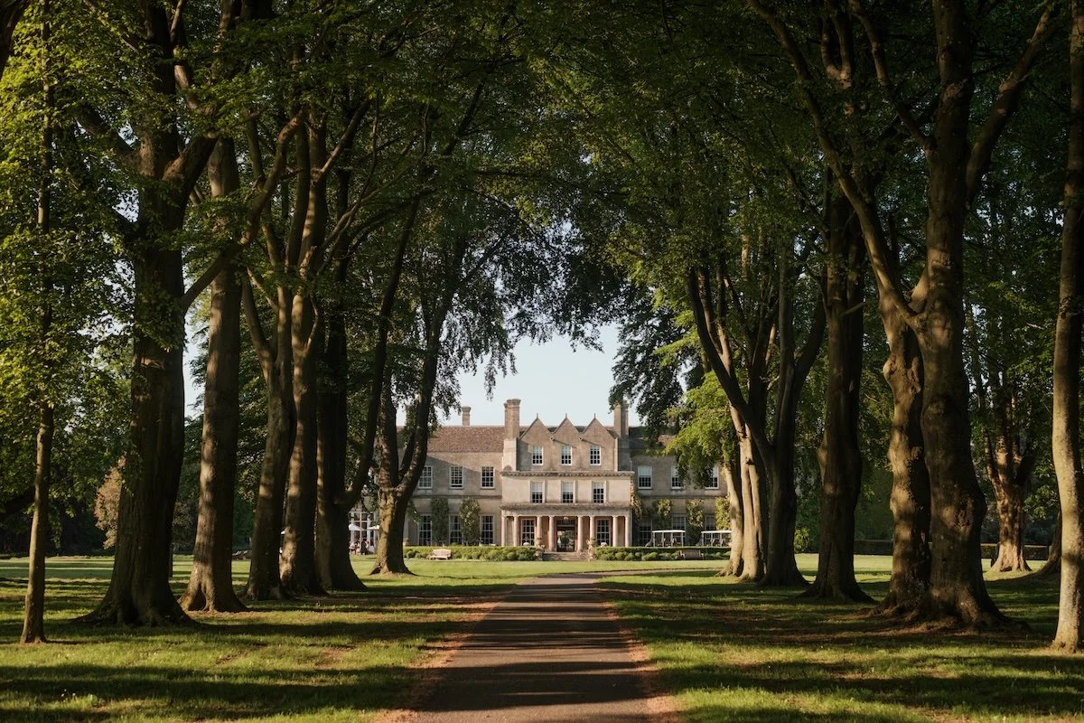 The stone facade of Lucknam Park Hotel, viewed from a distance through an avenue of trees