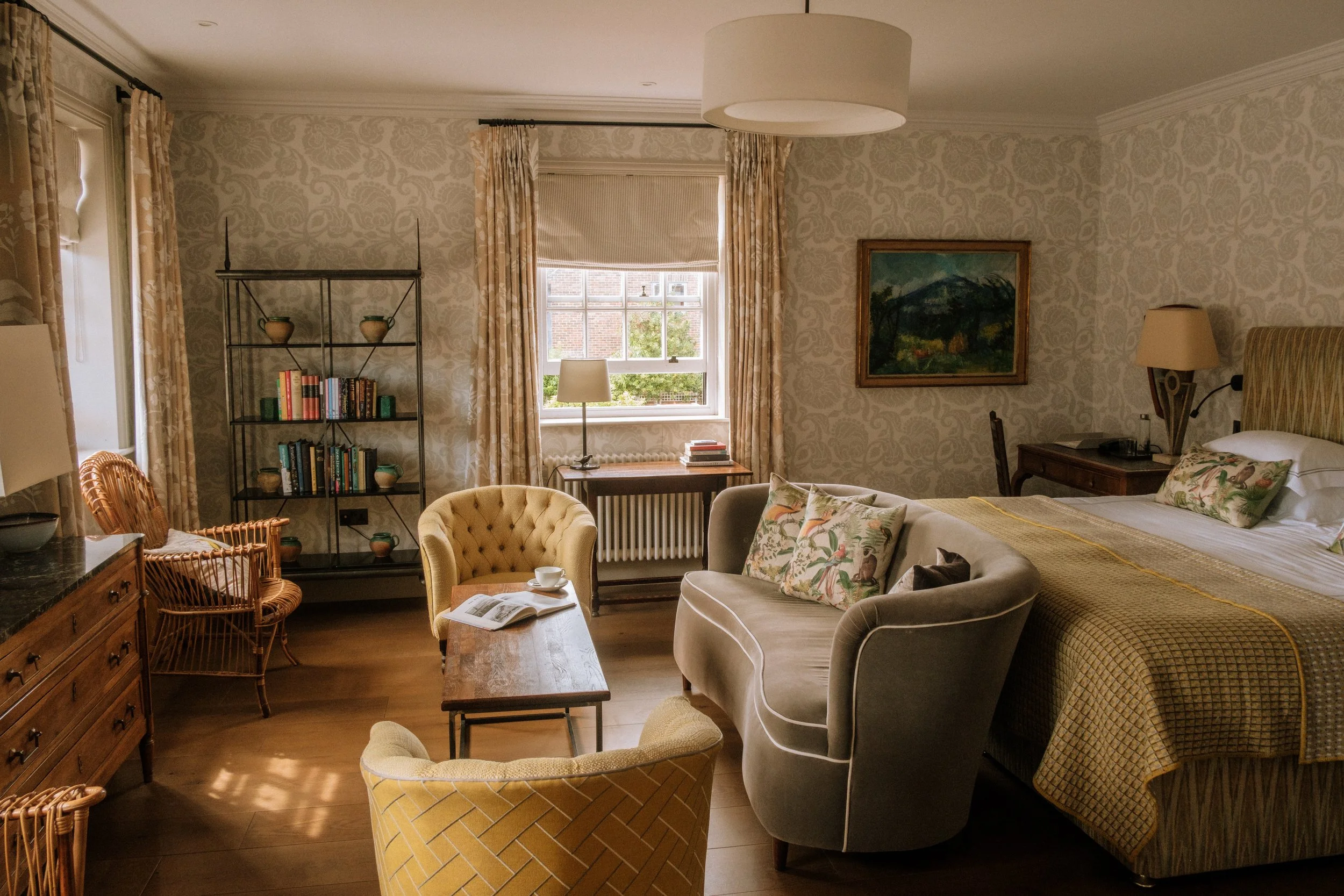 An interior shot of a bedroom at The Star in East Sussex. Furnishing come in yellow and cream, vintage art hangs on the wall and there is a floral pattern in the wallpaper