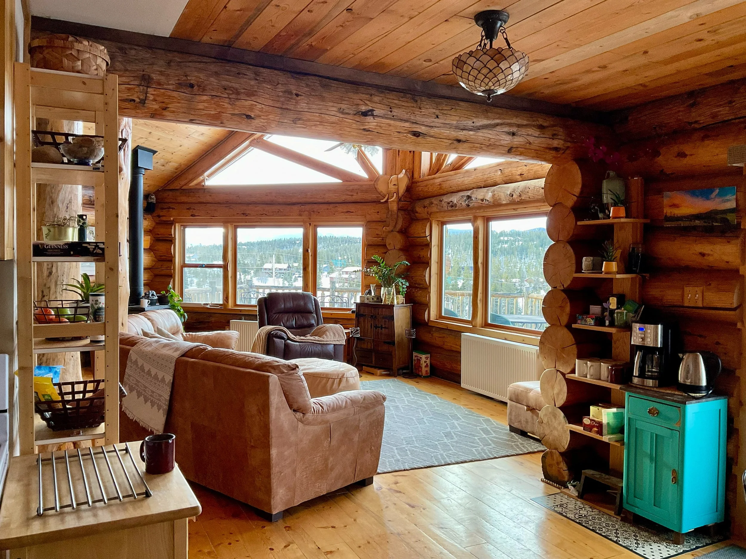 Great room interior with vaulted log cabin ceiling, wood stove, and mountain views through large windows
