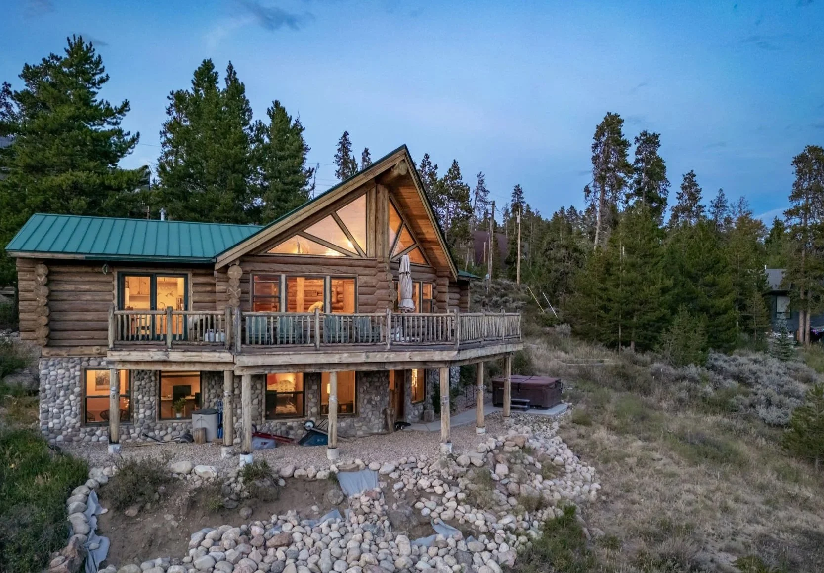Log cabin exterior at twilight with illuminated deck and mountain backdrop near Winter Park, Colorado