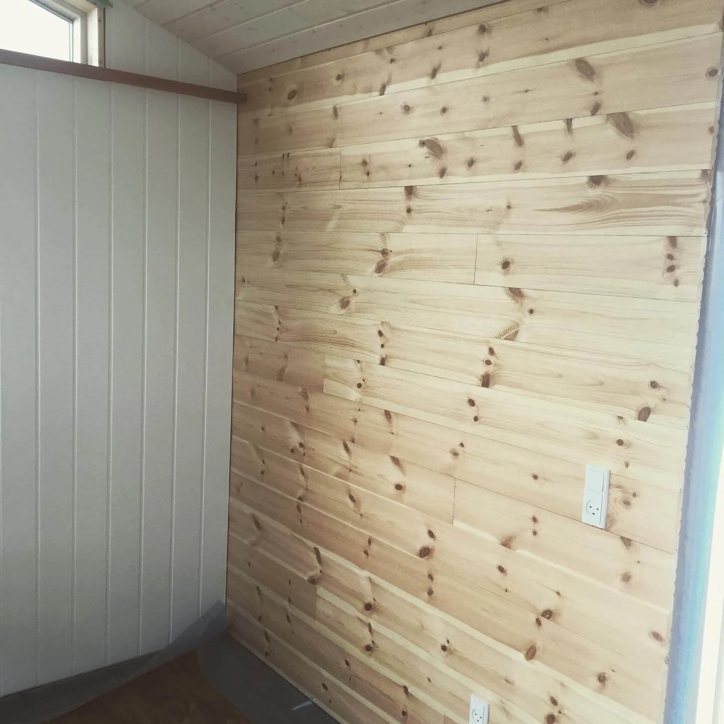 Tre af væggene er beklædt med hvidt huntonit, mens den fjerde væg står i natur for at bryde det hvide.