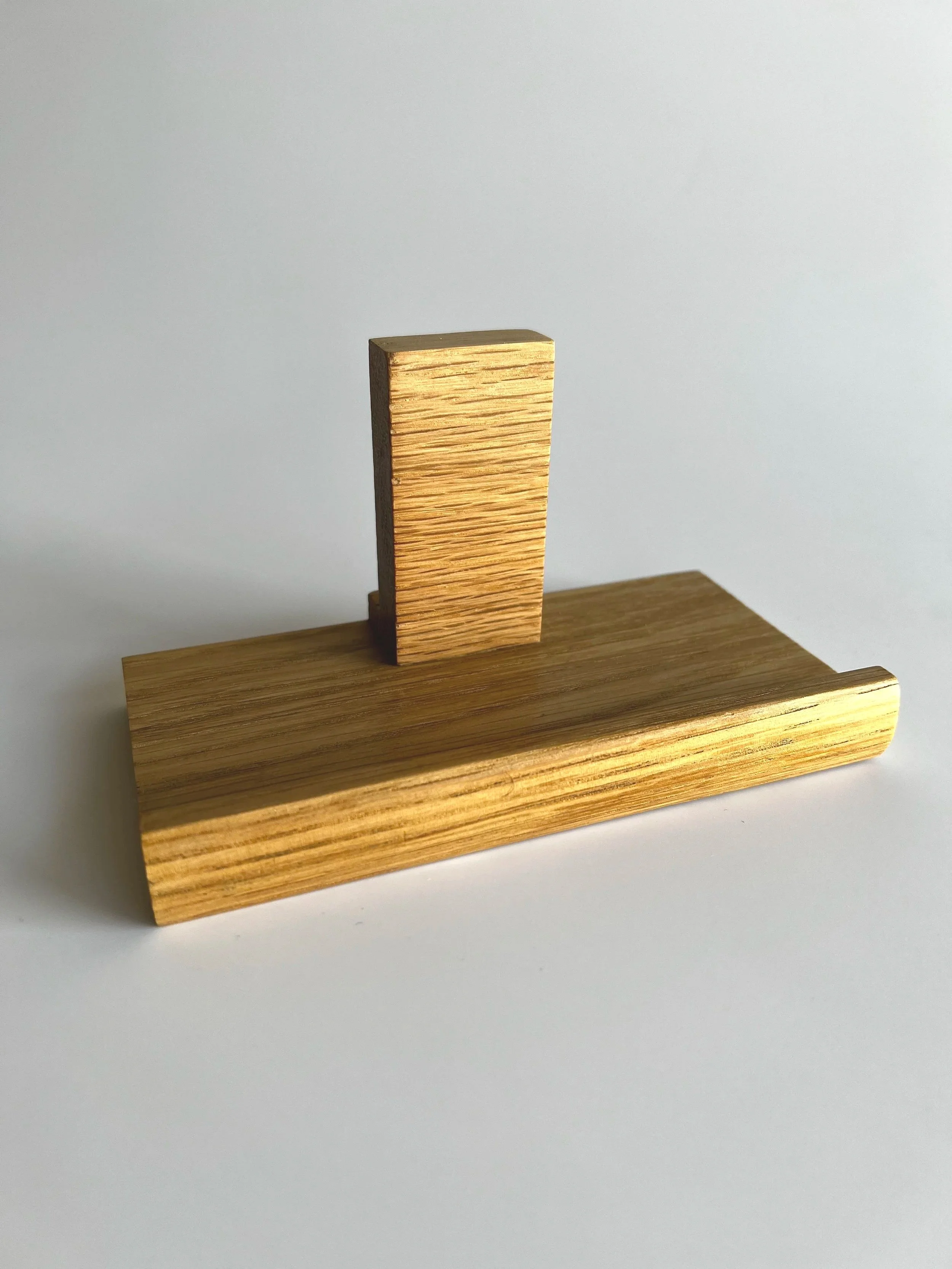 Two wooden blocks positioned on a white background, one upright and one lying flat, forming an abstract minimalist sculpture.