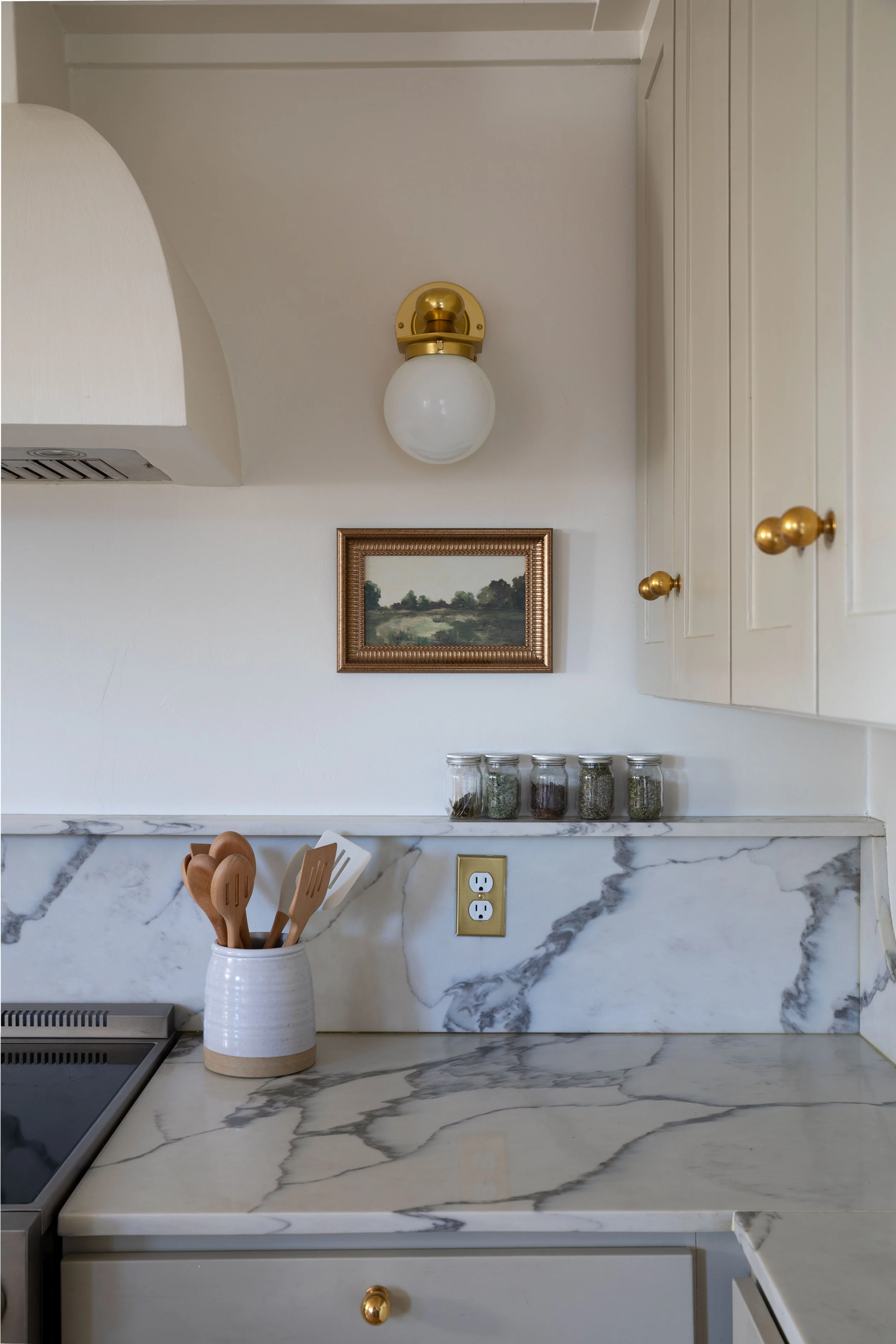Close-up of corner with brass sconce, framed artwork, and quartz backsplash with shelf.