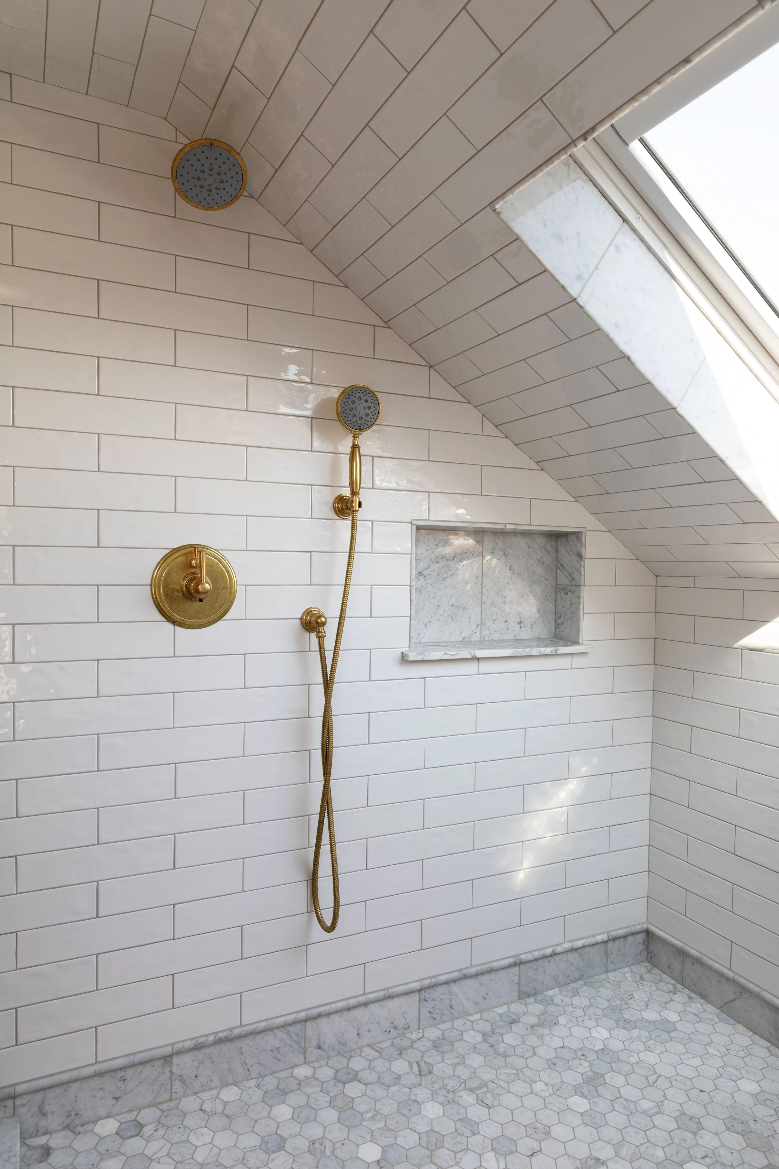 White and marble shower in the Hill House ensuite bathroom with brass shower set and handheld shower