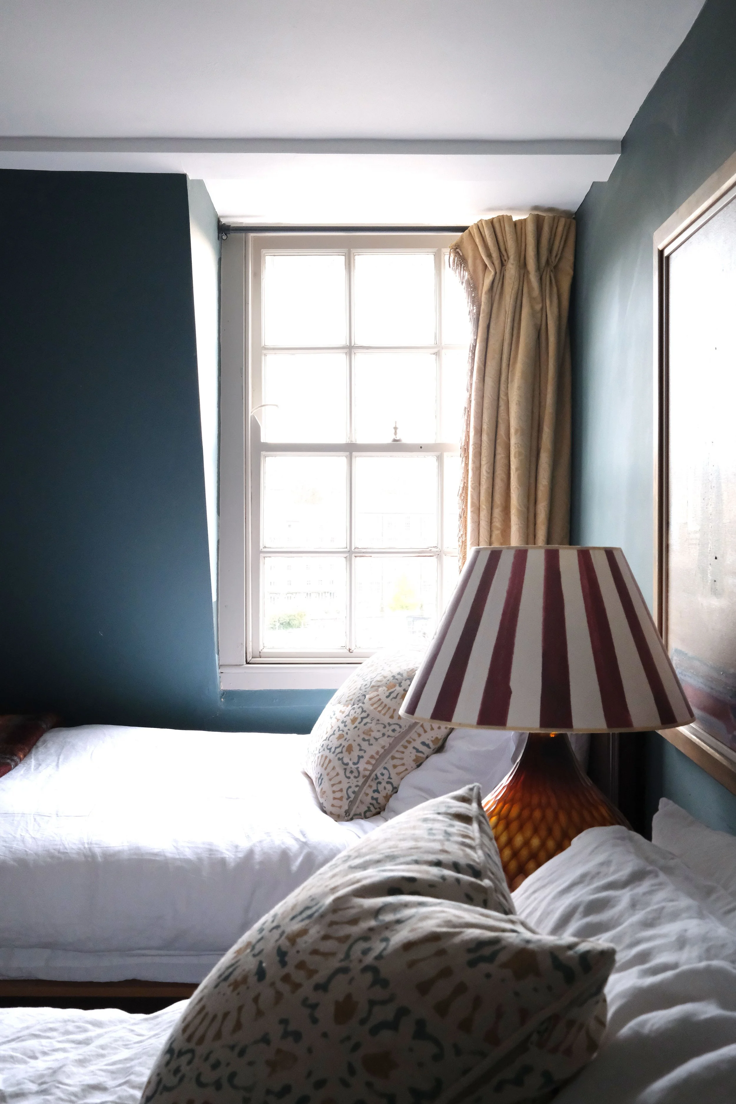 Deep blue-green bedroom with twin beds, vintage artwork, and antique furniture