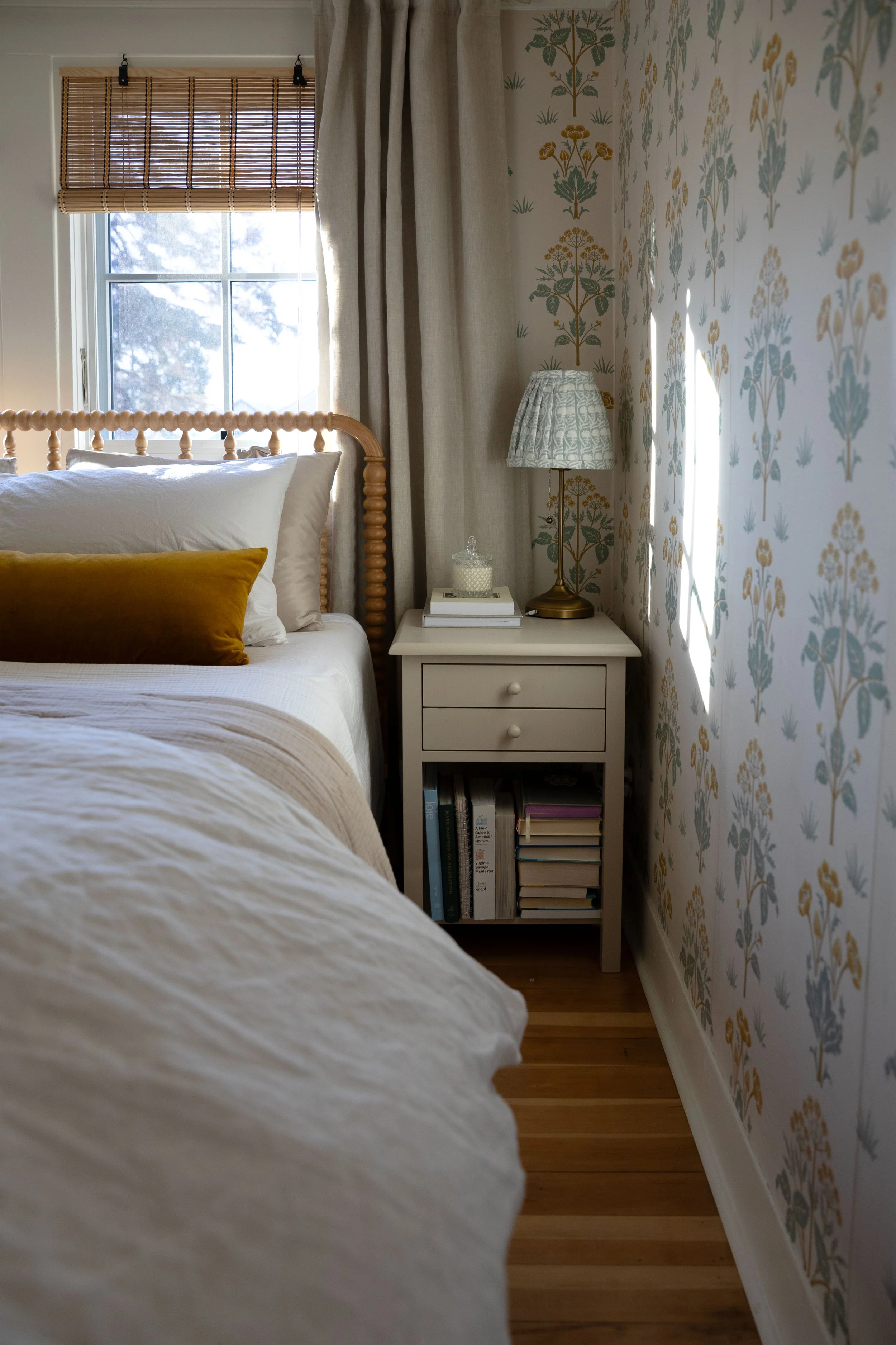 Cozy cottage bedroom with layered cotton and linen bedding, wallpaper, and soft window