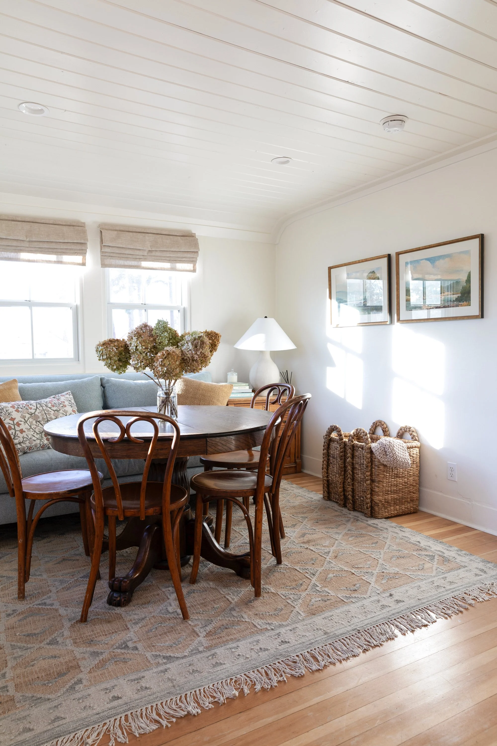 Side view of sitting and dining room with wood-clad windows, bentwood chairs, floor lamp, and blue sofa