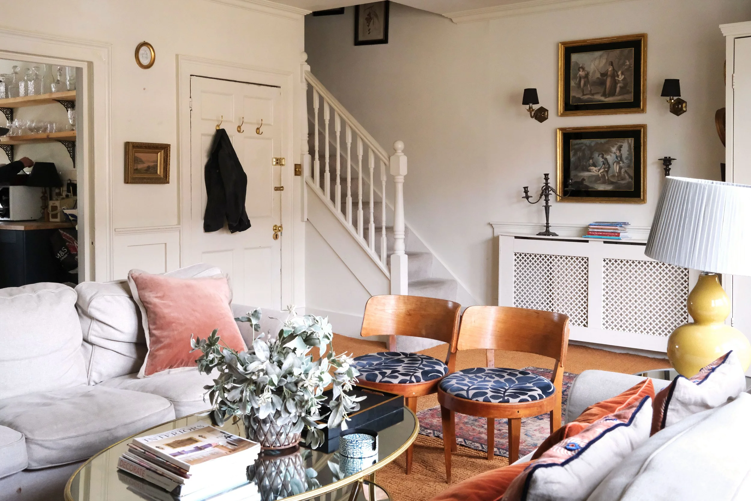 White living room in a historic Bath apartment with vintage art, antique furniture, and layered rugs