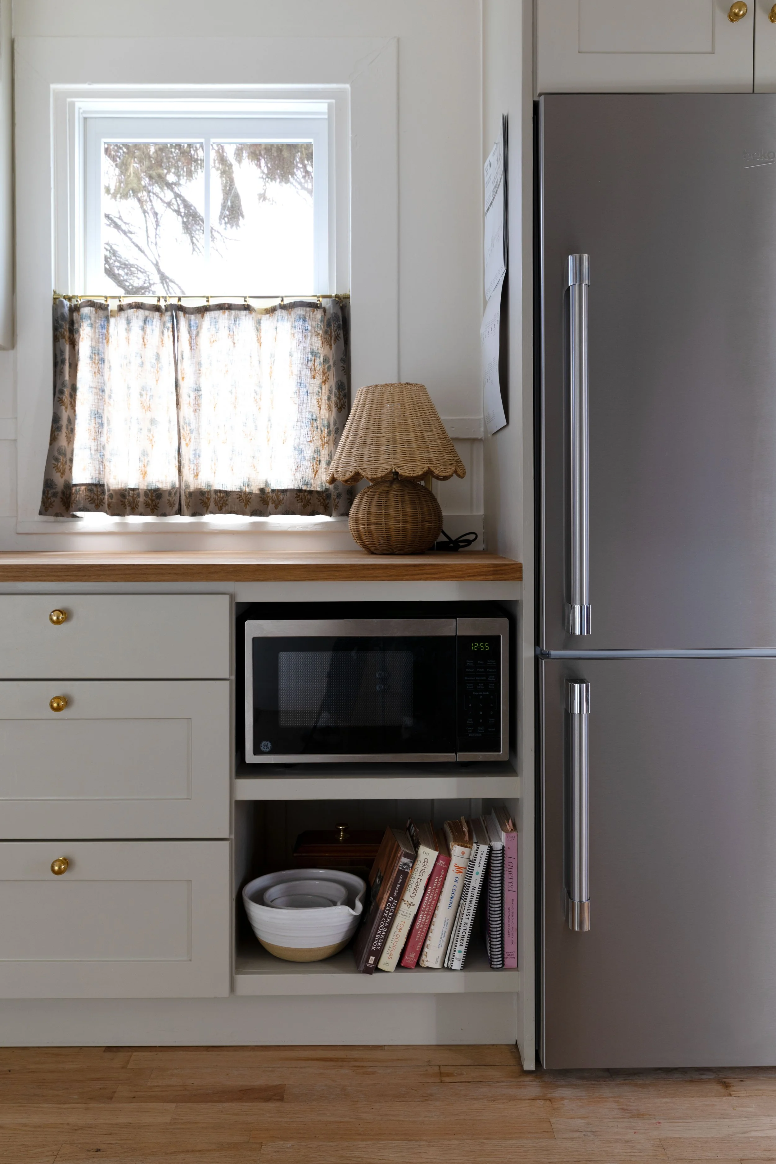 Close-up of built-in microwave shelf with bowls and cookbooks below.