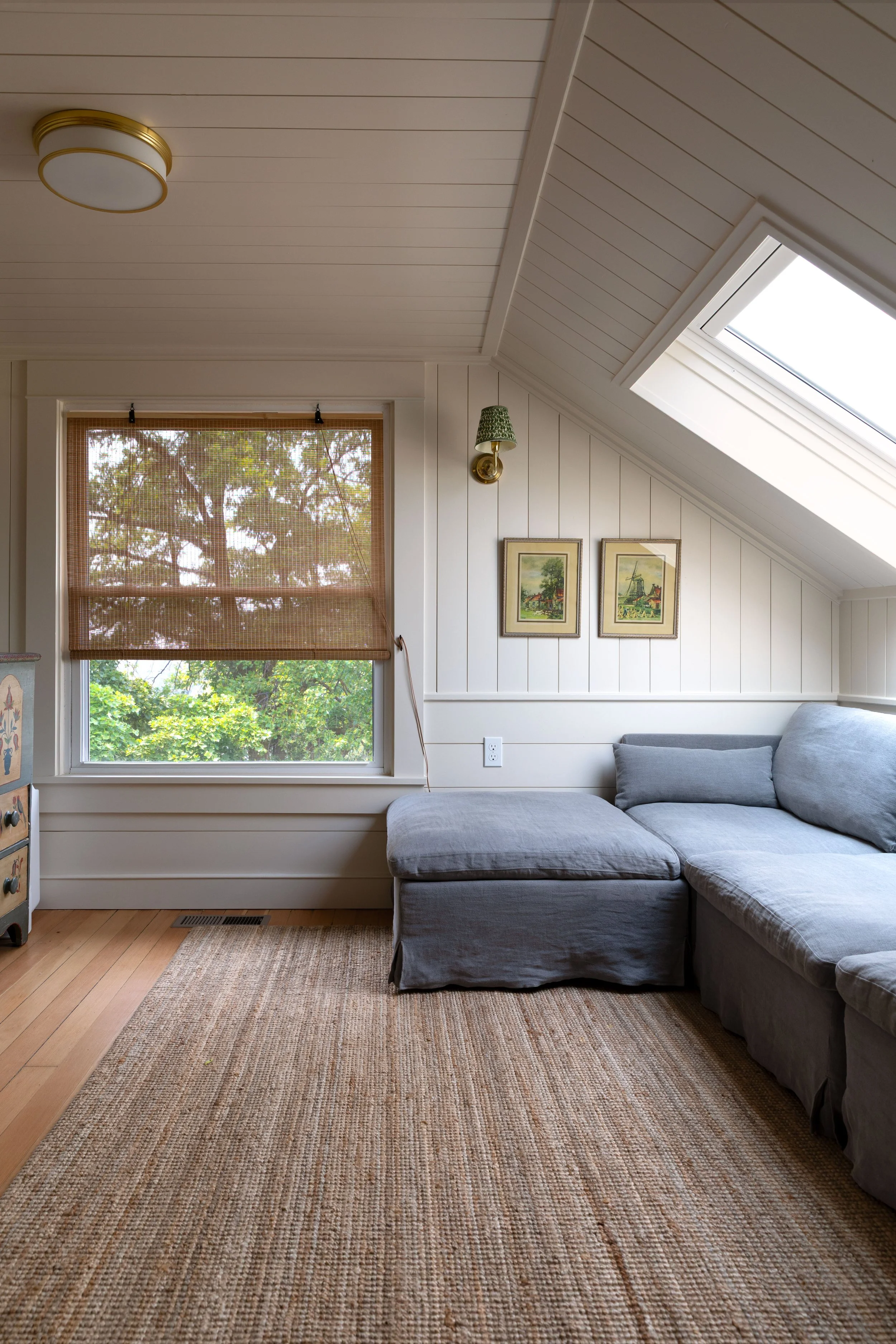 Small upstairs snug with linen sectional, skylight, reading sconce, and paneled walls
