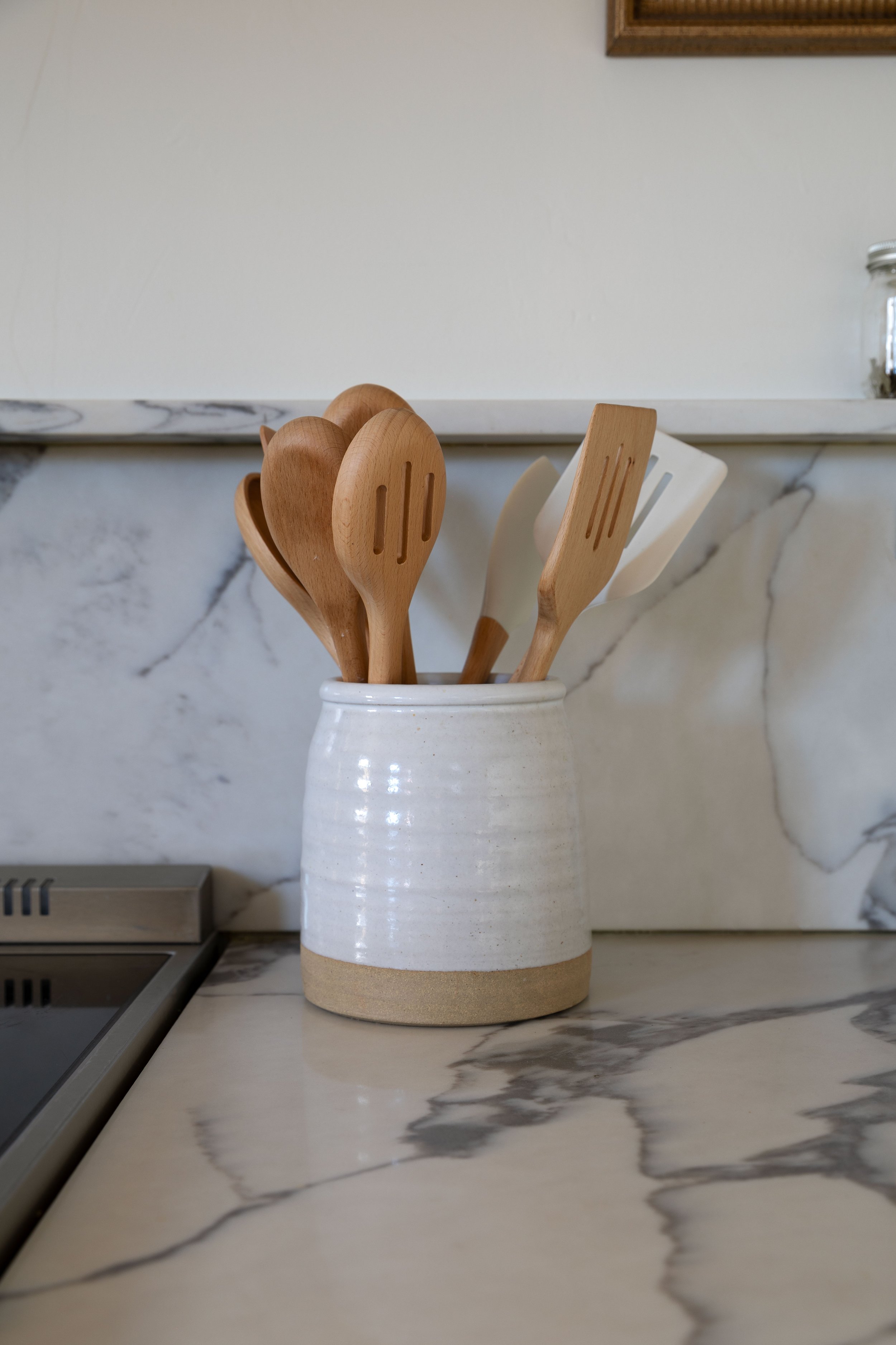 Stoneware crock filled with wooden spoons on countertop.
