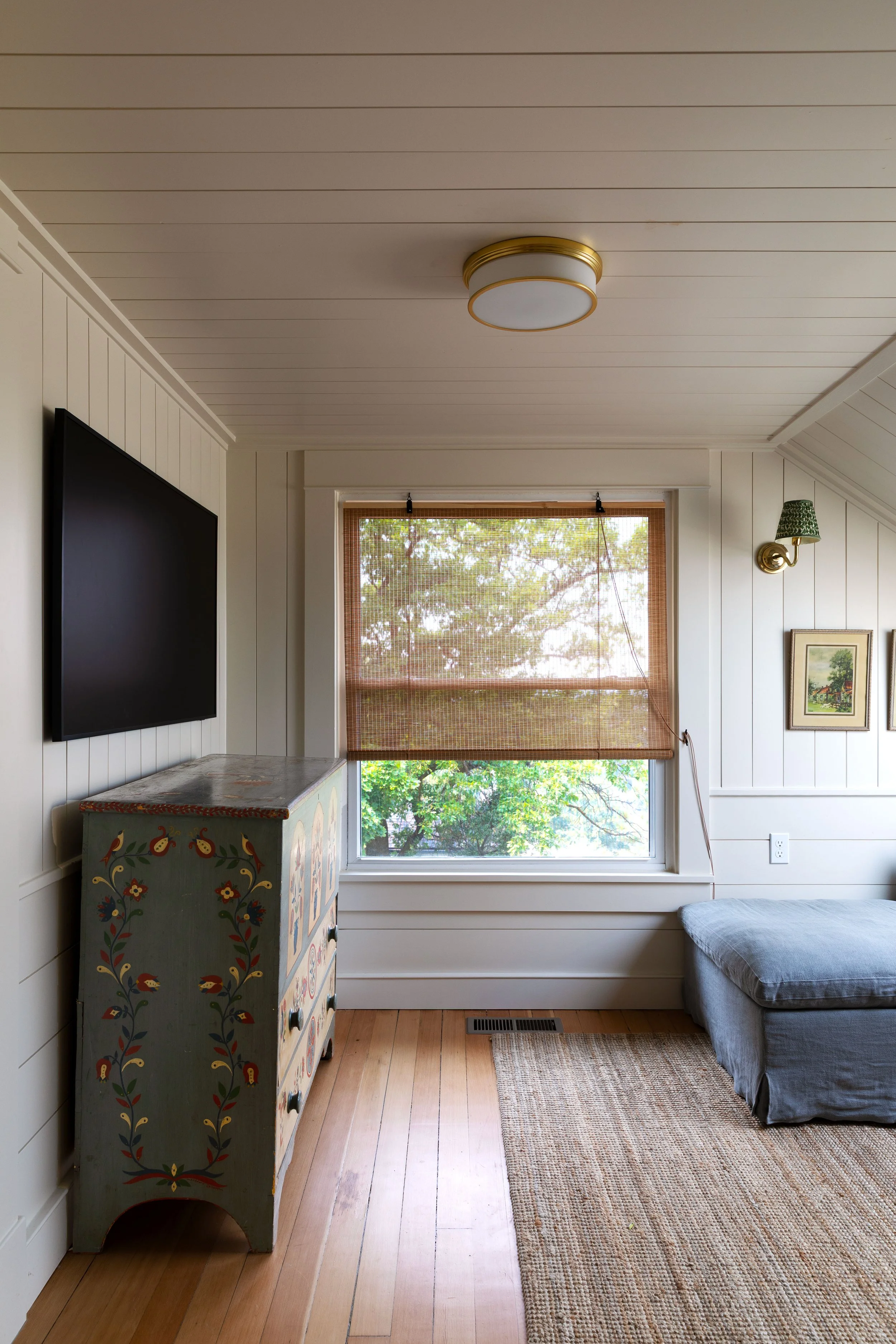Small old-house upstairs snug with painted vintage dresser, woven shade, and wood floors