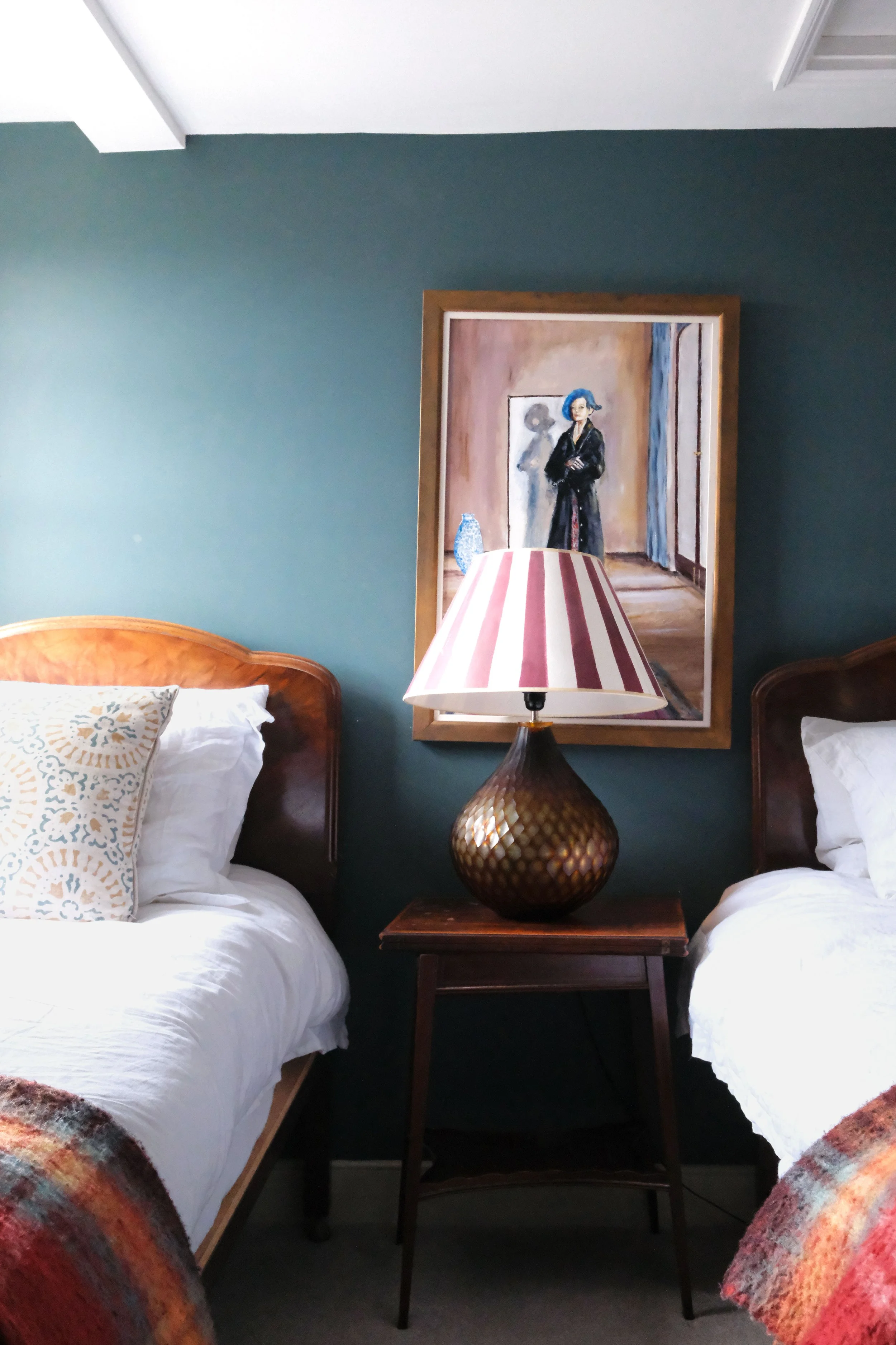 Deep blue-green bedroom with twin beds, vintage artwork, and antique furniture