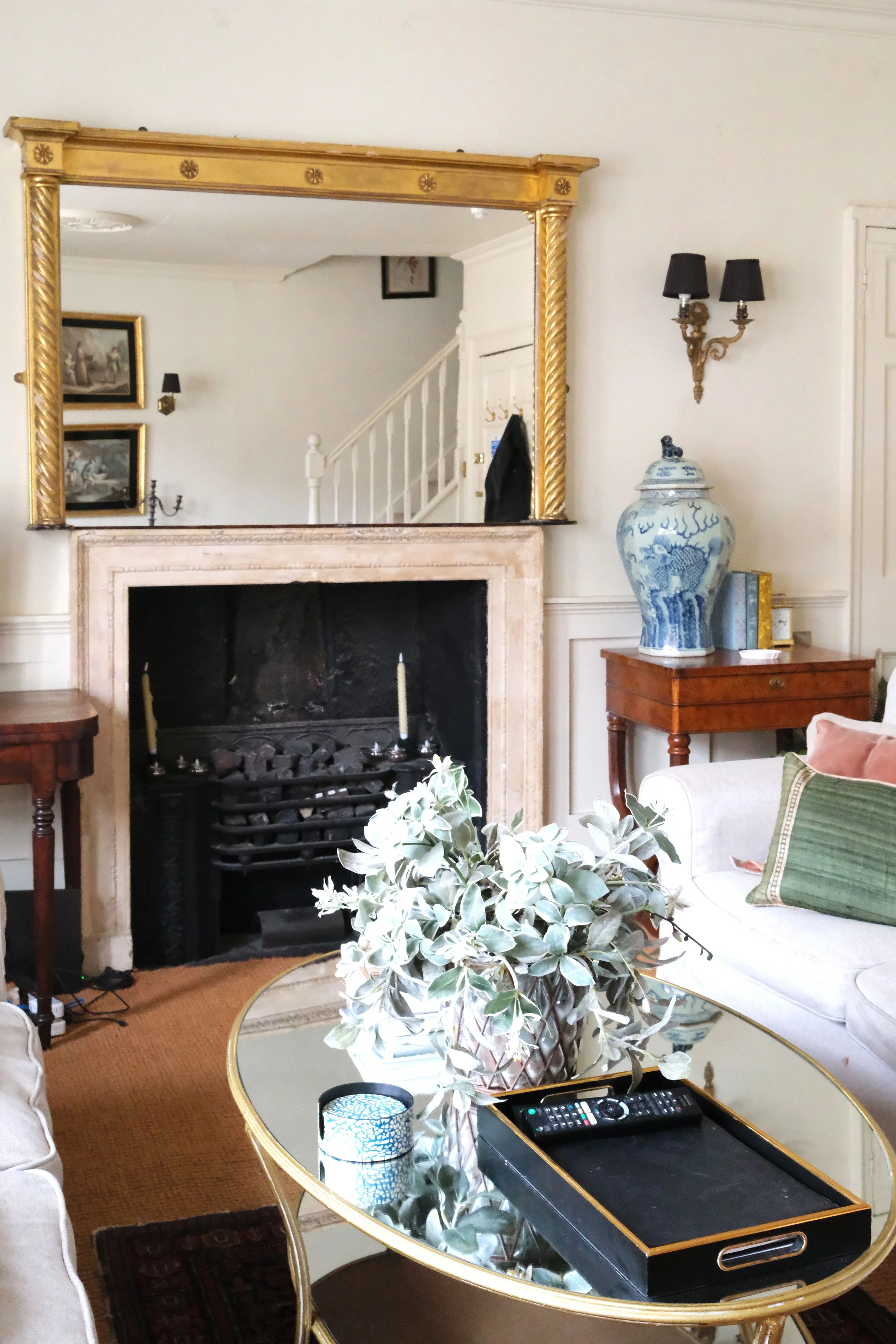 White living room in a historic Bath apartment with vintage art, fireplace, and layered rugs