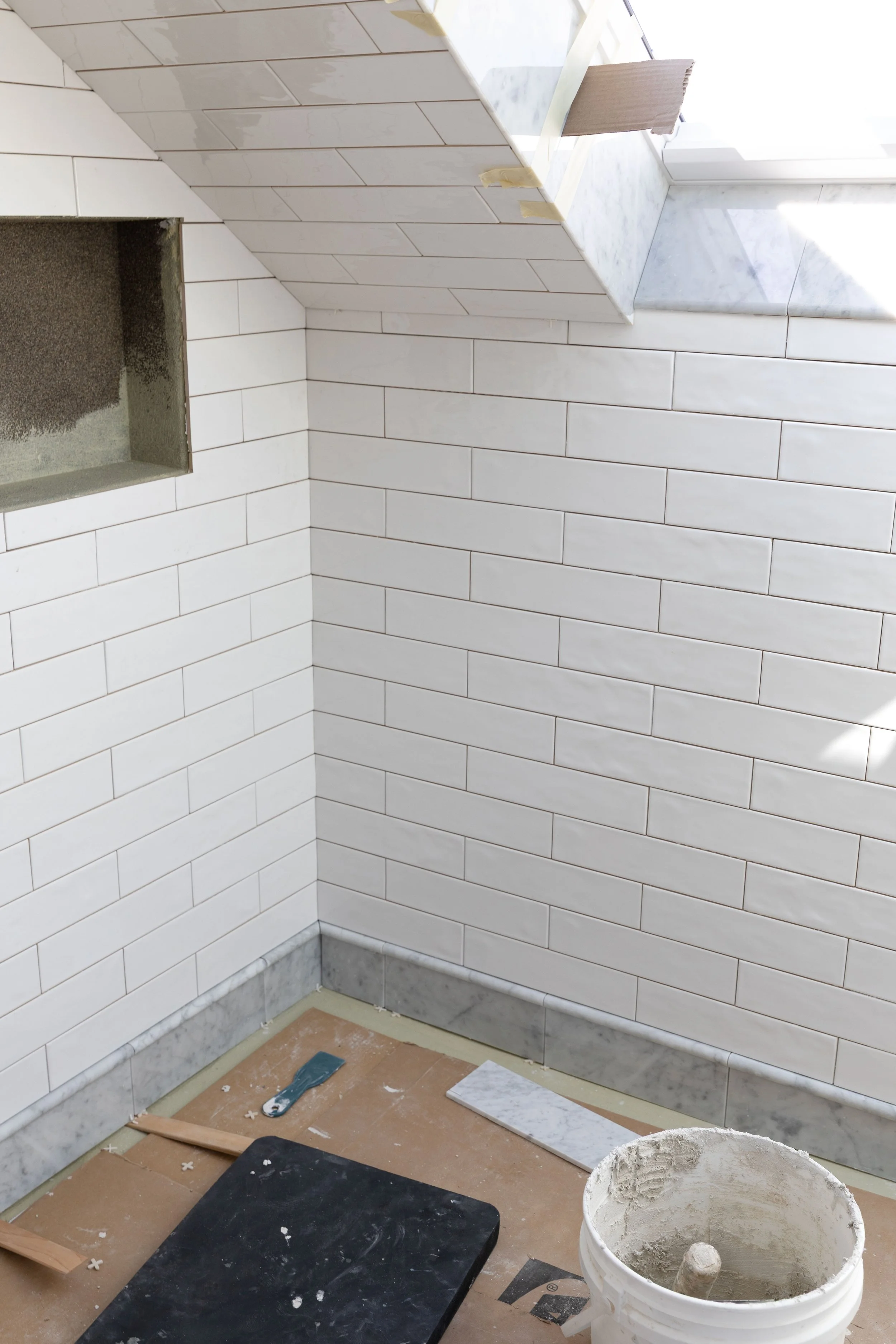 A tiled wet room with white subway tile walls and ceilings and a marble base