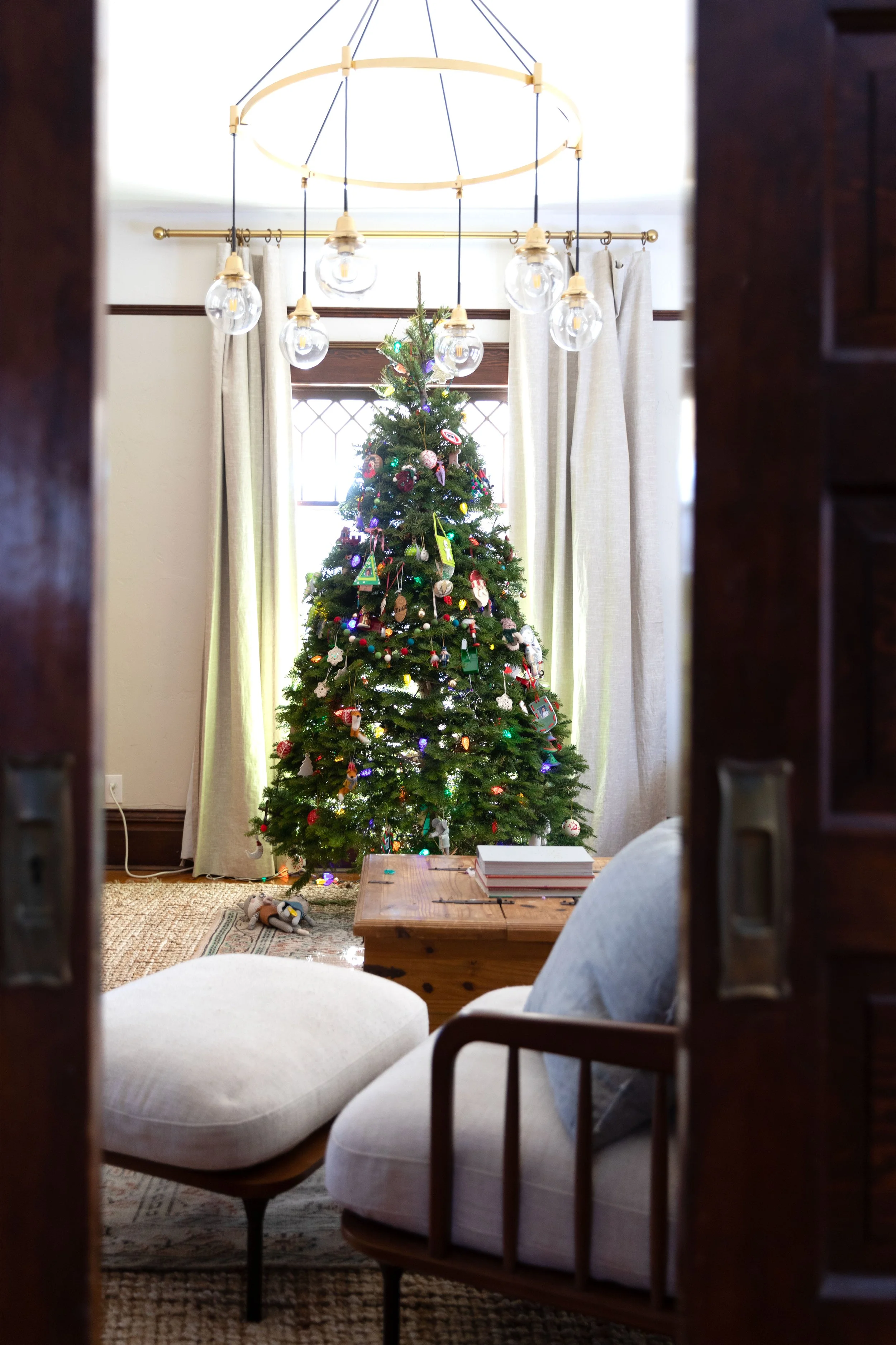 Historic farmhouse living room with a classic Christmas tree, vintage ornaments, and warm wood tones — cozy old-house holiday style.