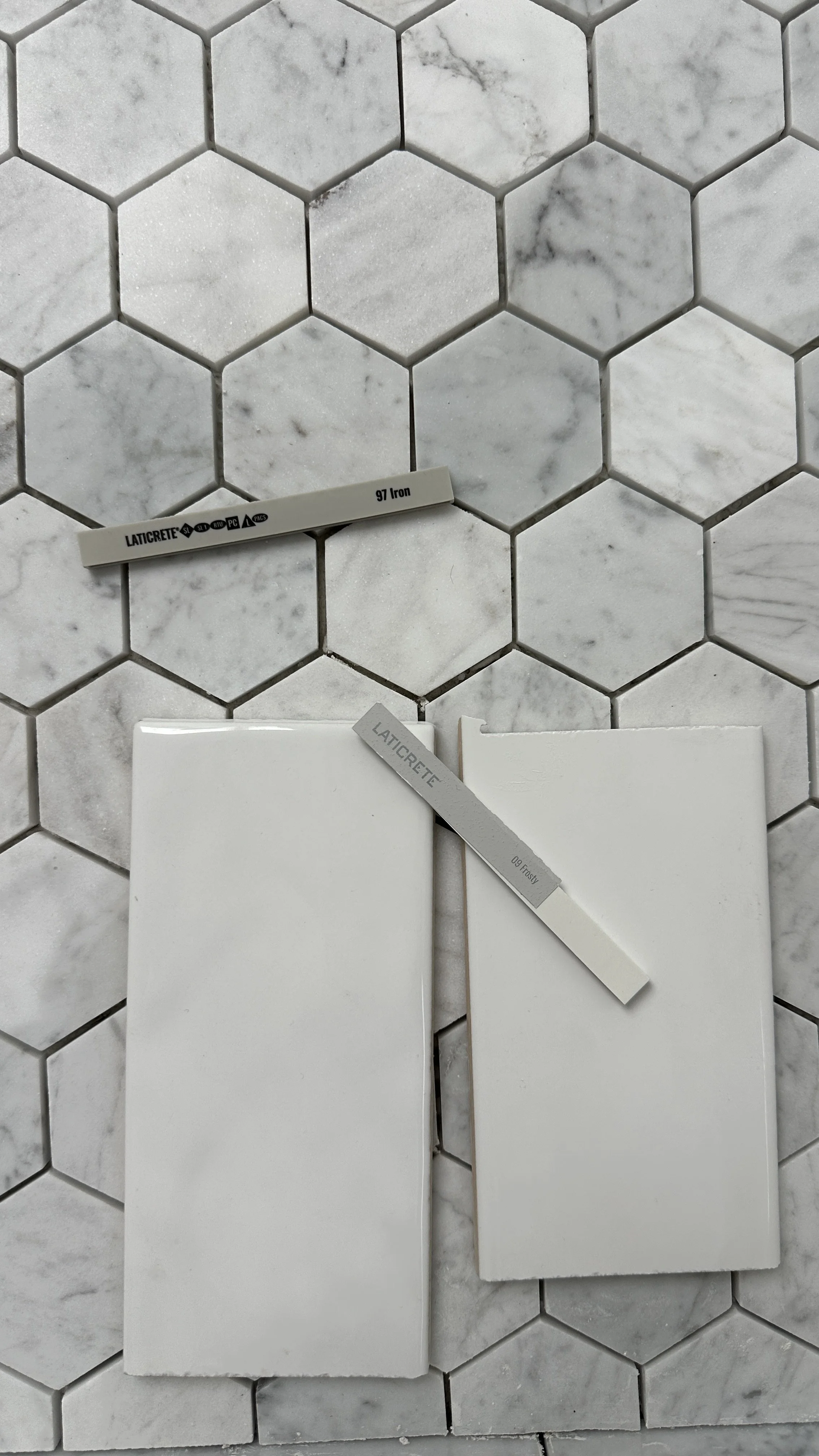 Close up of laticrete spectralock epoxy grout color samples iron and frosty with white and marble tiles