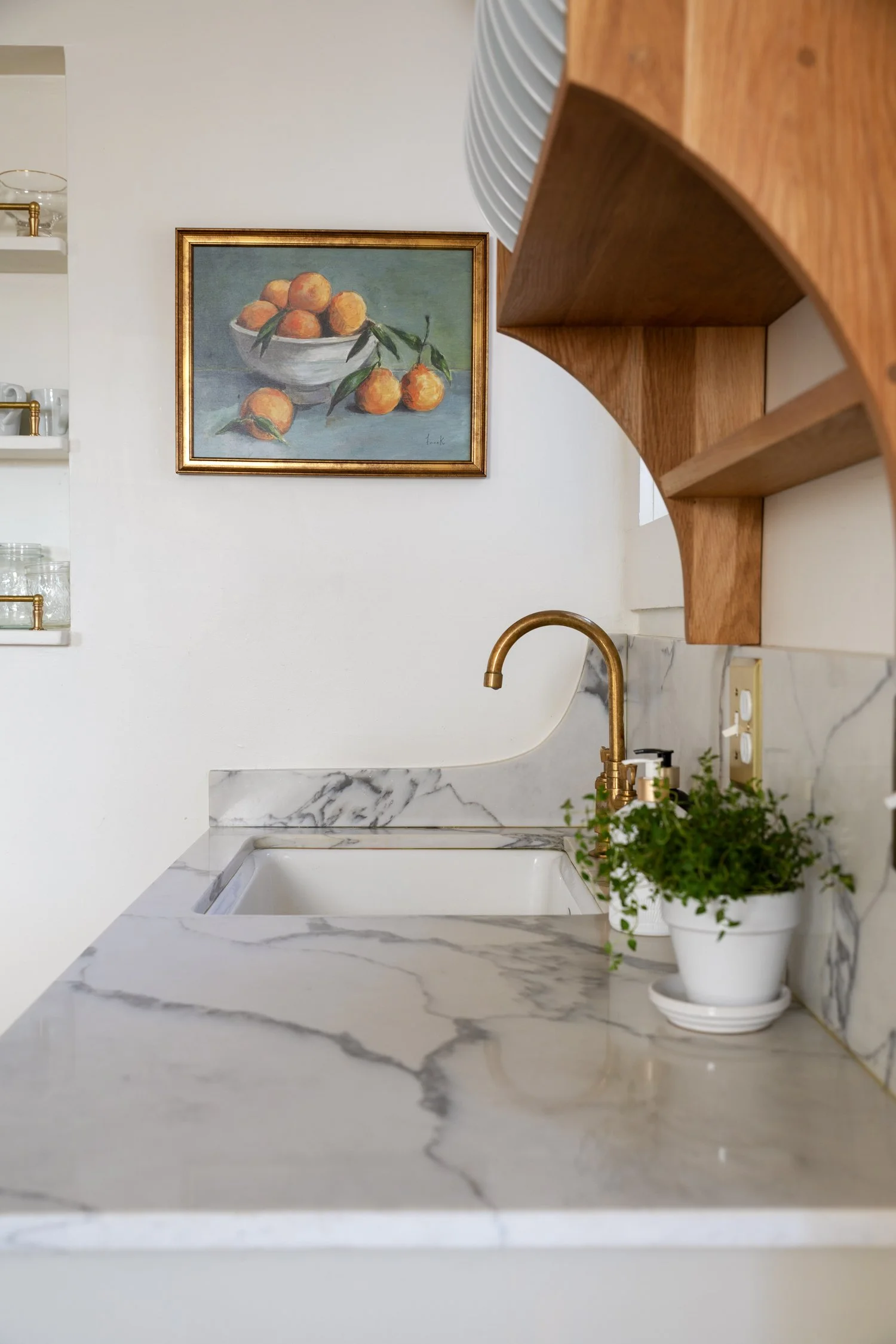 Close-up of brass faucet, quartz backsplash curve, plate rack edge, and artwork.