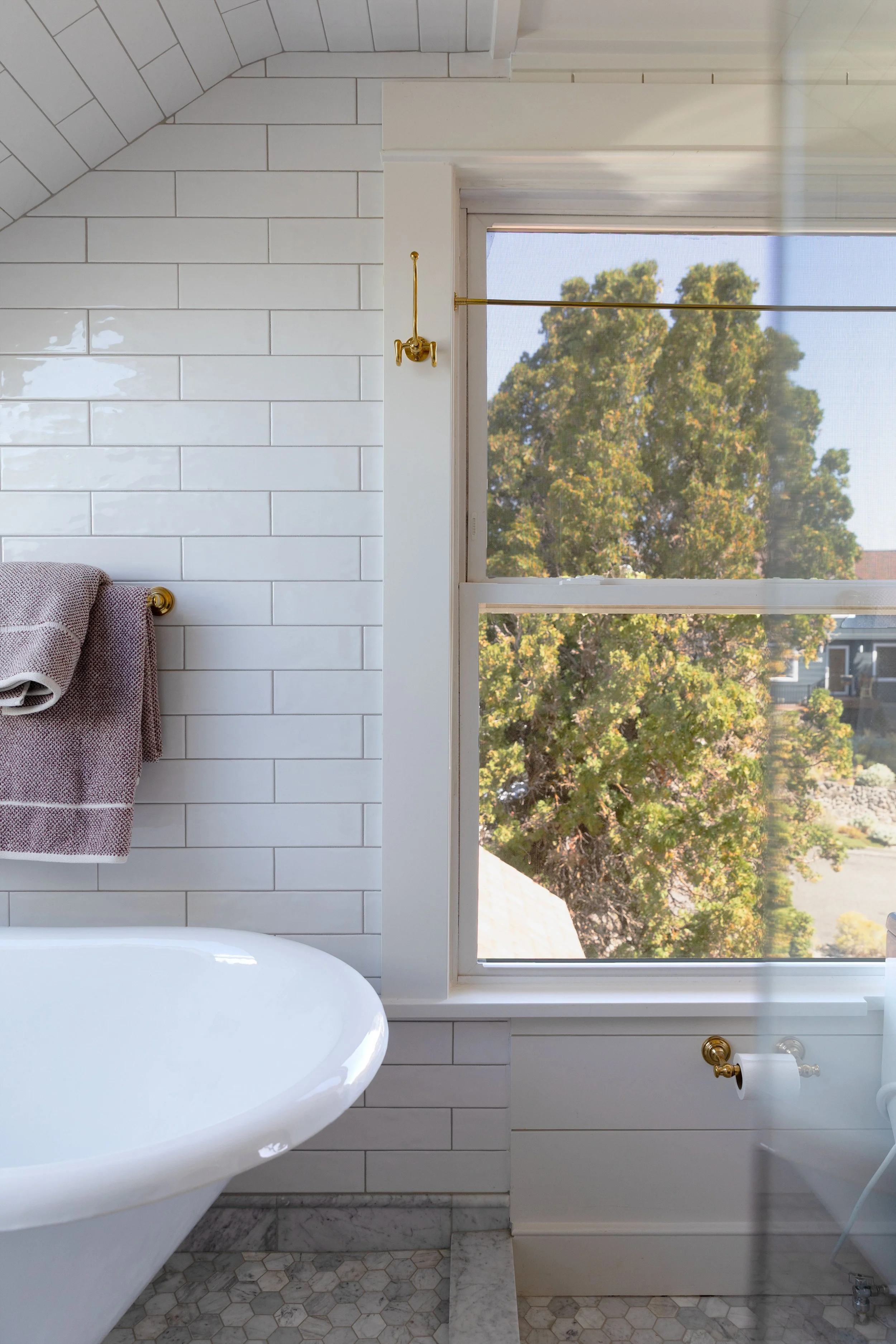 Clawfoot tub beside a tall bathroom window with a brass cafe curtain rod