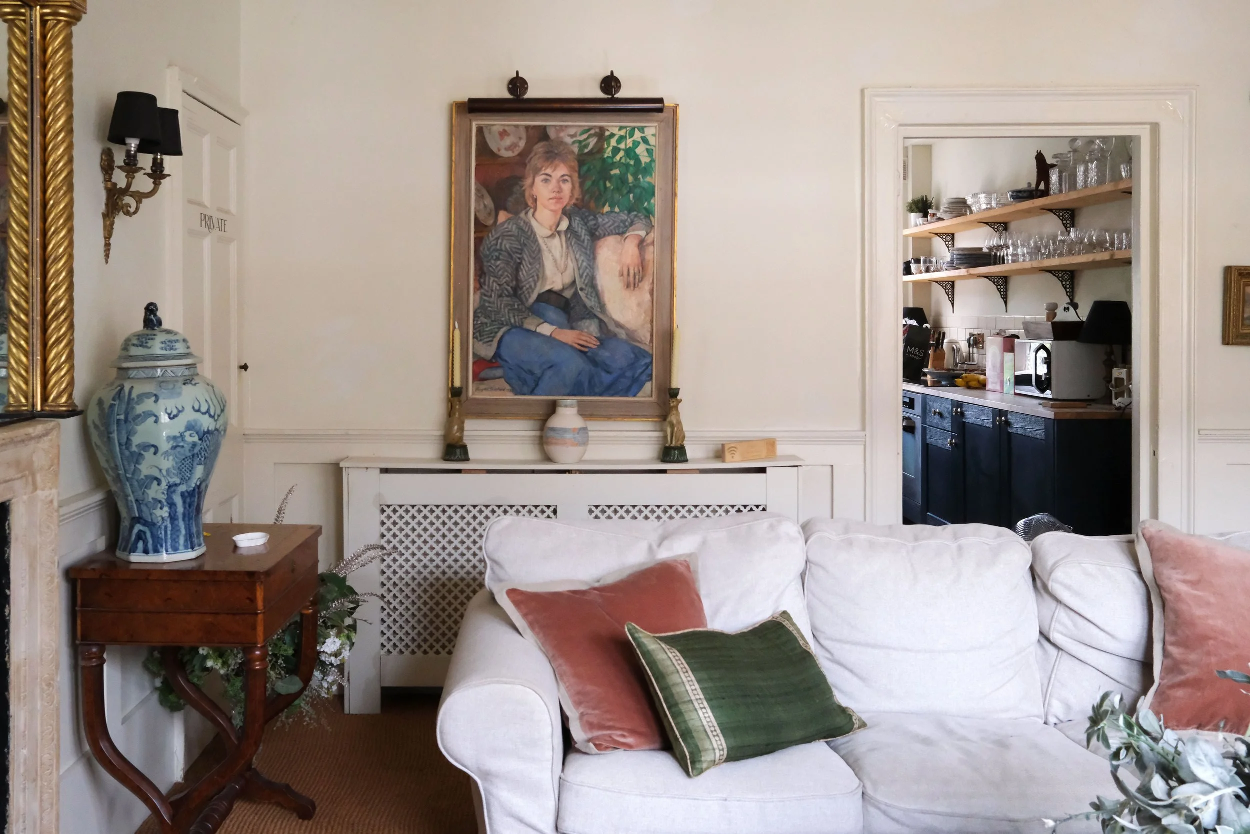 Comfortable white sofa surrounded by vintage paintings, books, brass lighting, and antique furniture