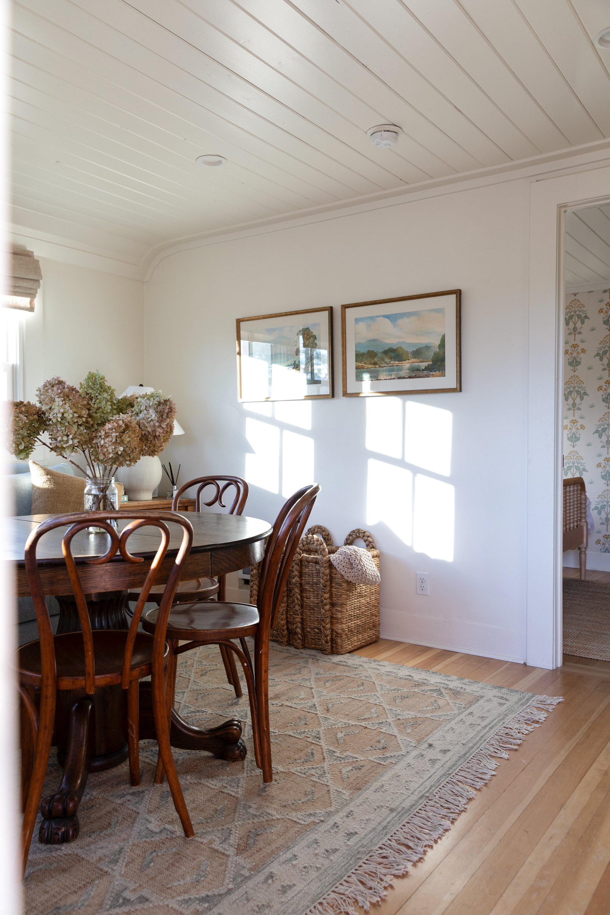 Angled view of small sitting and dining room layout with flatweave rug, vintage table, and bedroom doorway beyond