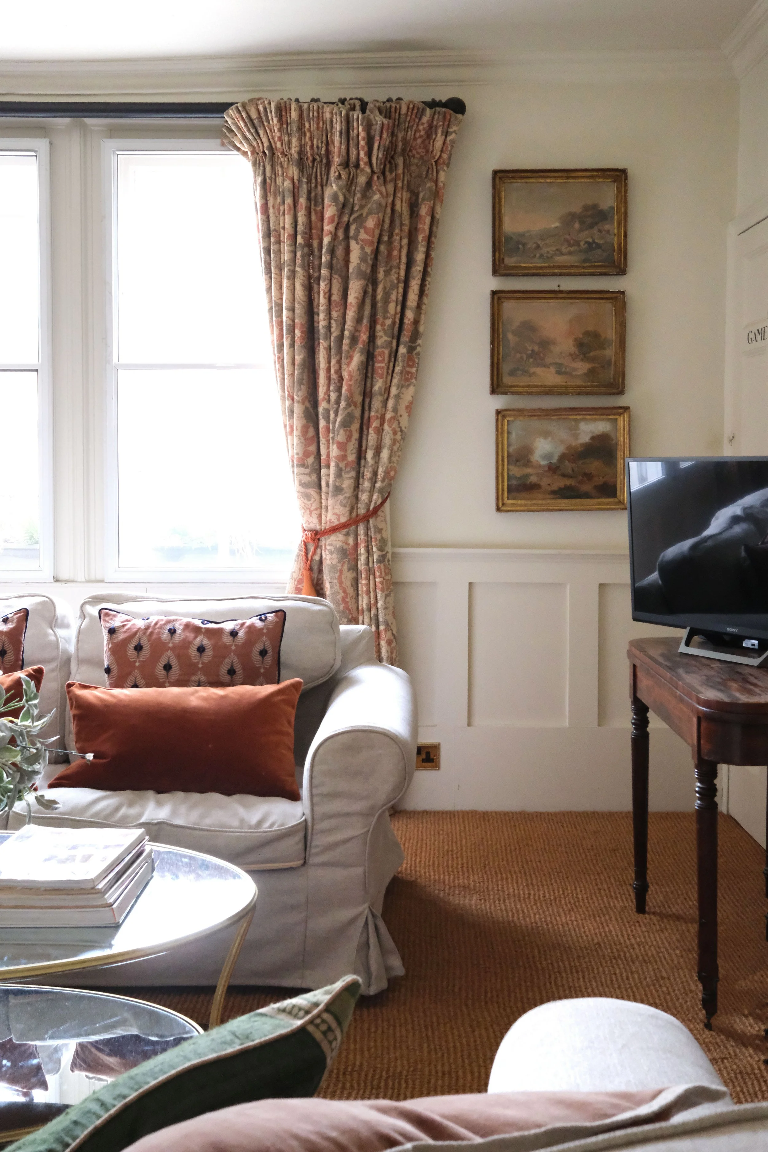 Comfortable white sofa surrounded by vintage paintings, books, brass lighting, and antique furniture