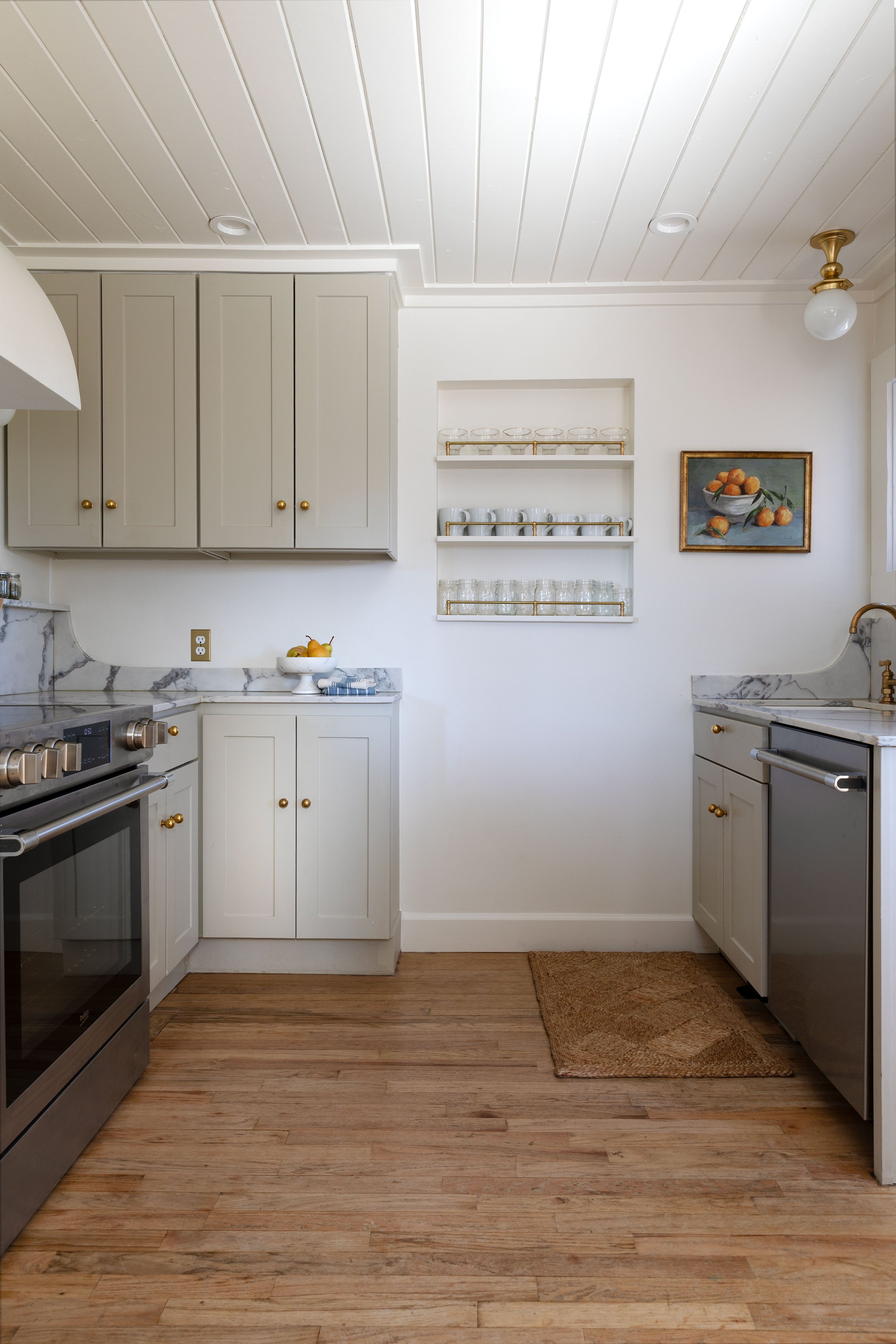 Wide view of the Poplar Cottage kitchen with recessed shelves, brass gallery rail, and painted cabinets.