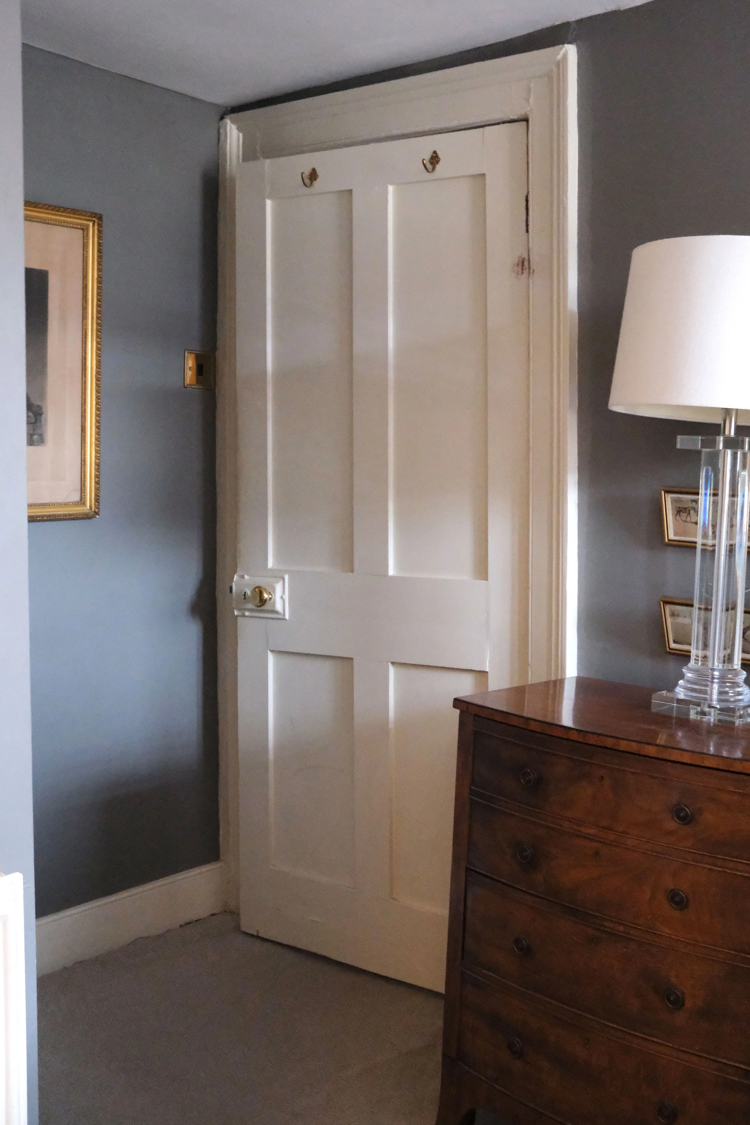 Soft gray bedroom with antique portraits, brass details, and dark wood furniture