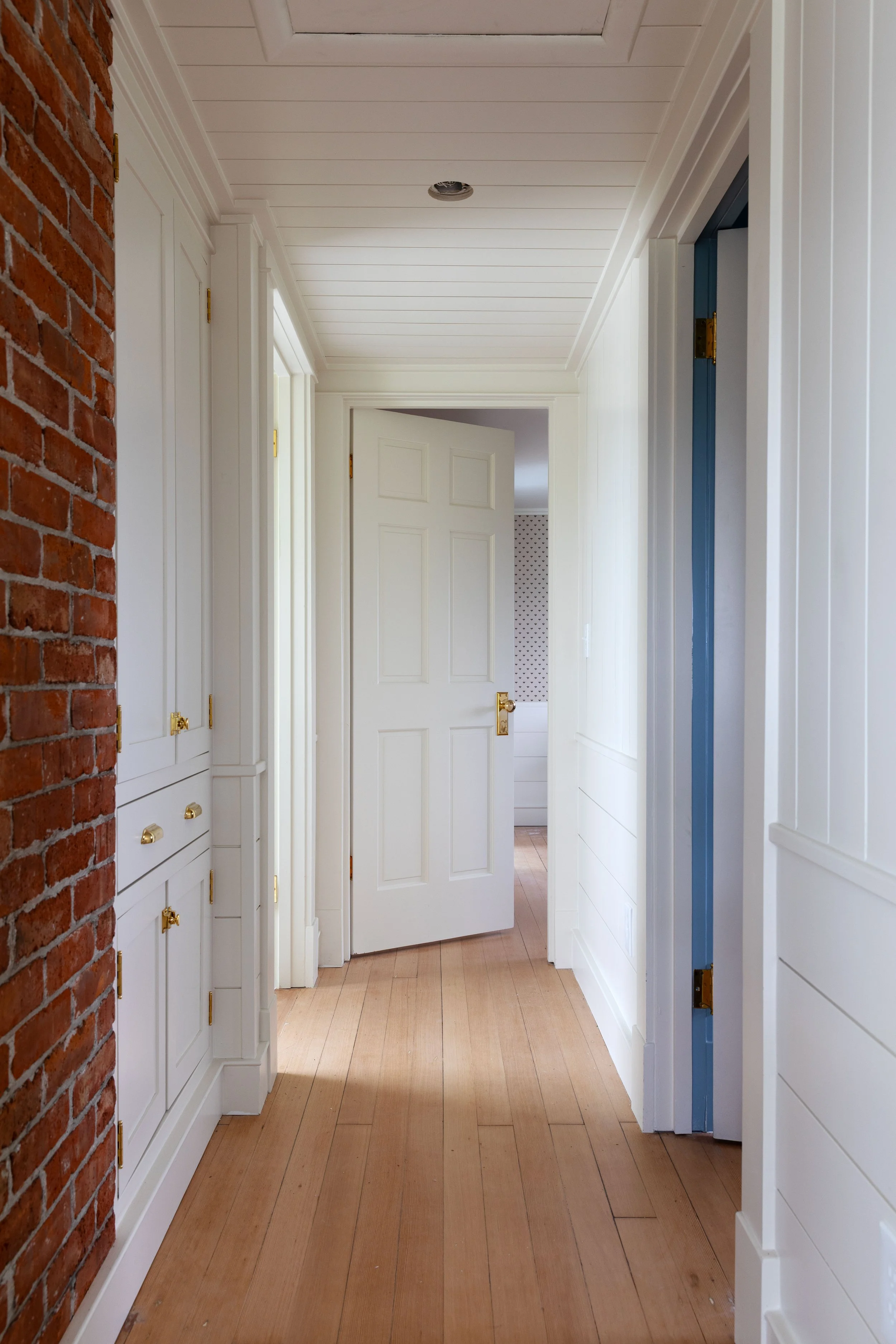 The Hill House upstairs hallway with vintage doors, brass hardware, refinished fir floors, and paneling