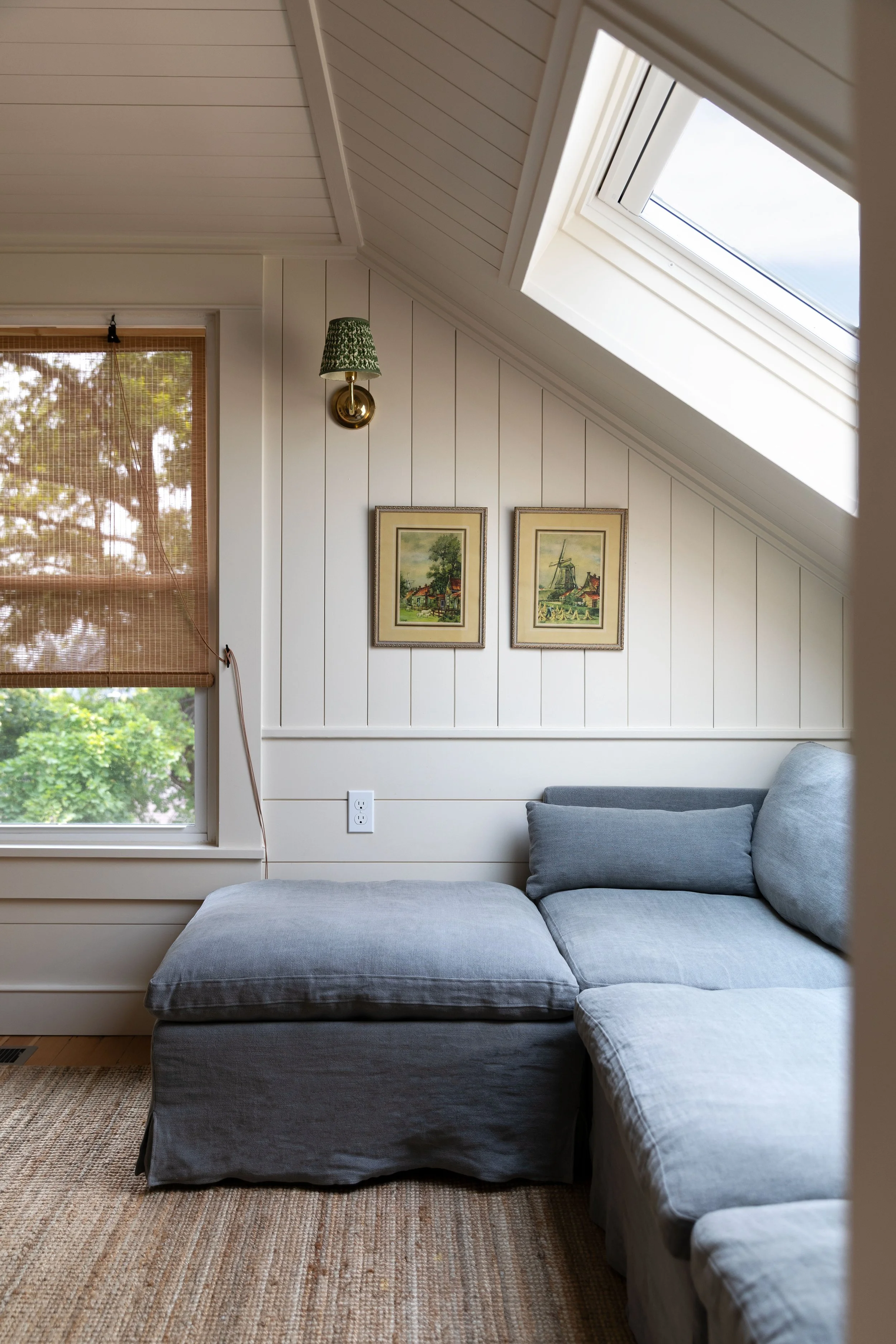 Small upstairs snug with linen sectional, skylight, reading sconce, and paneled walls