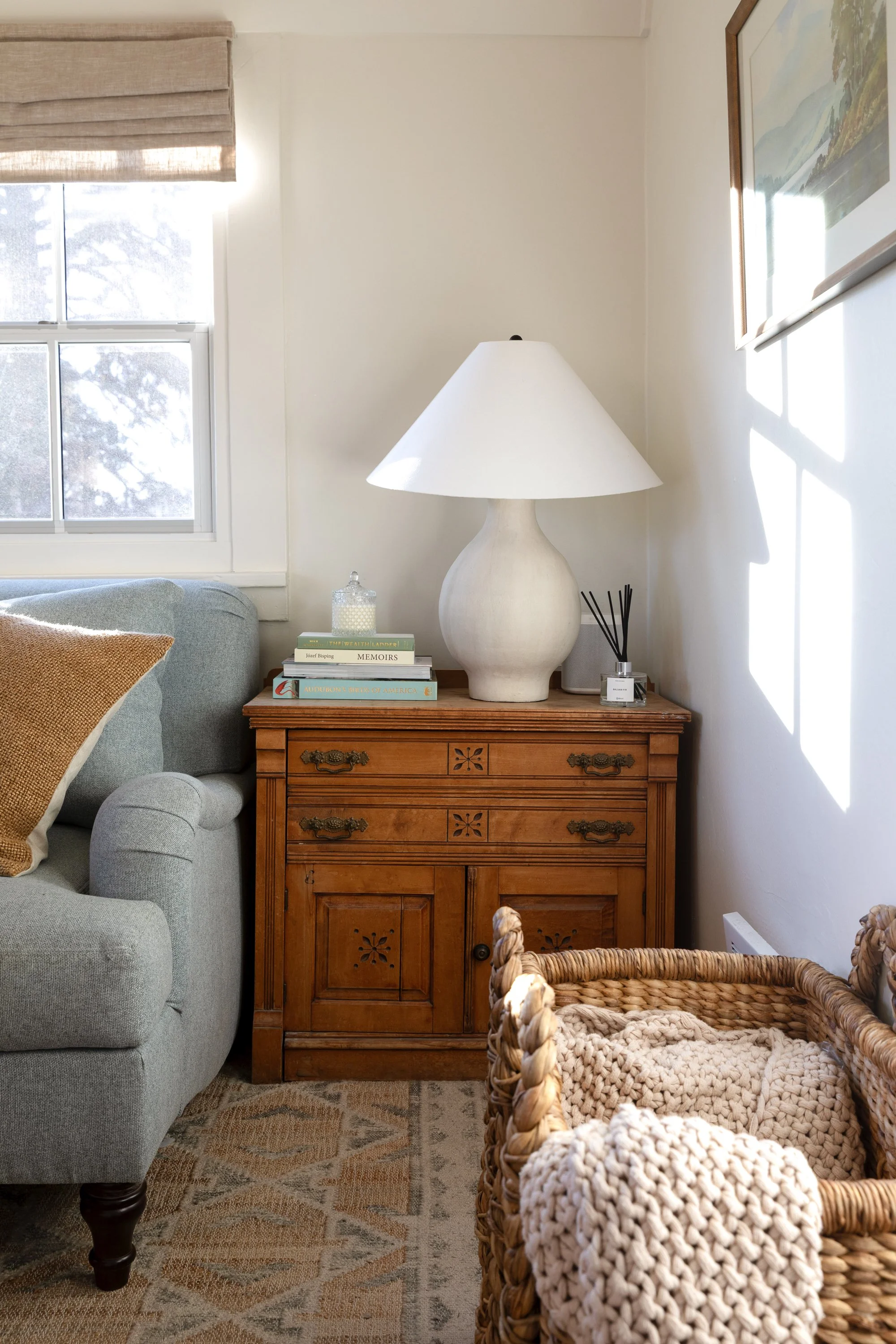Close-up of vintage side table with carved details, table lamp, books, and basket beside sofa in the Poplar Cottage