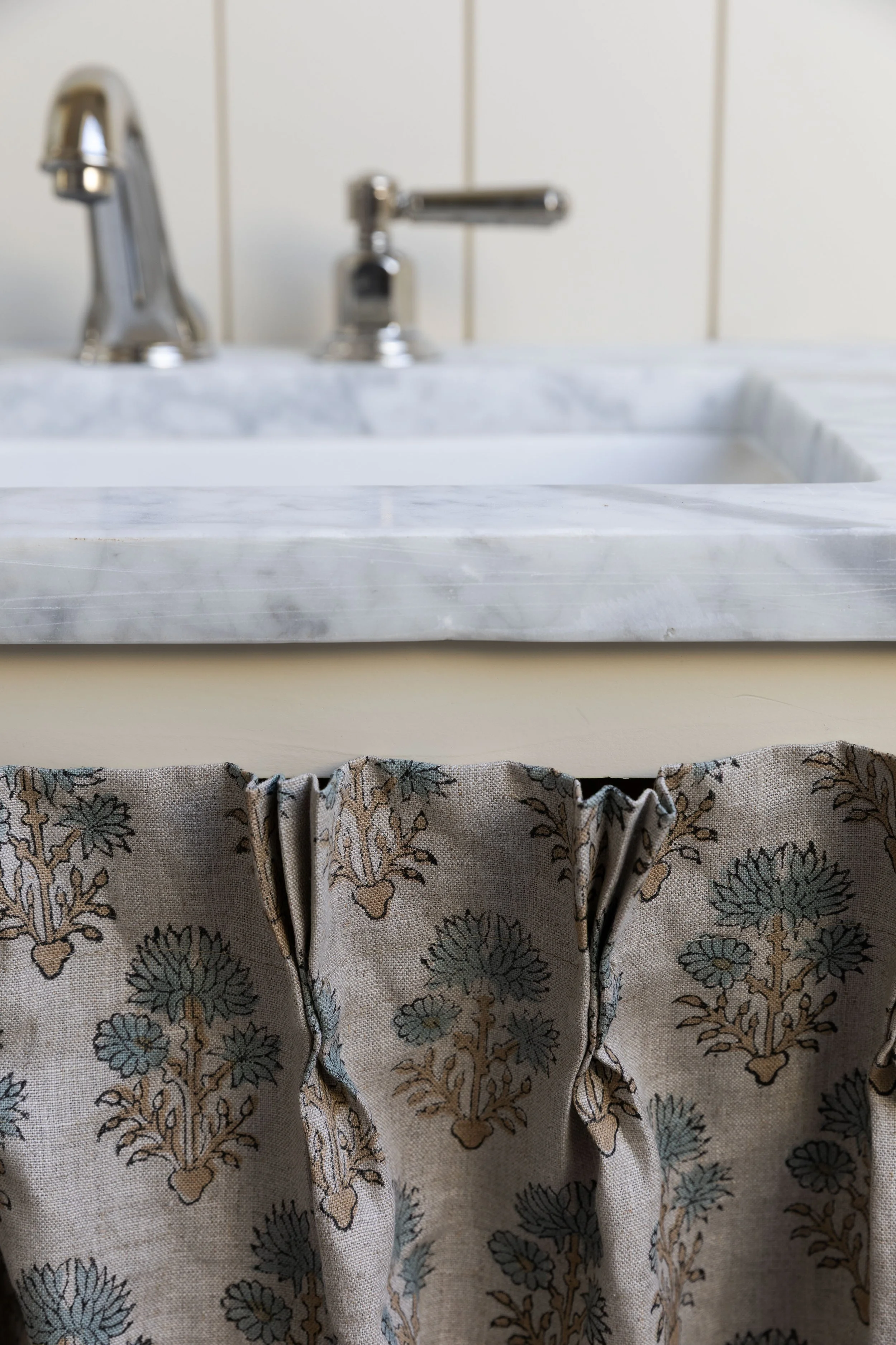 Detail of the skirted vanity in our Hill House hall bath with marble countertop and brass faucet