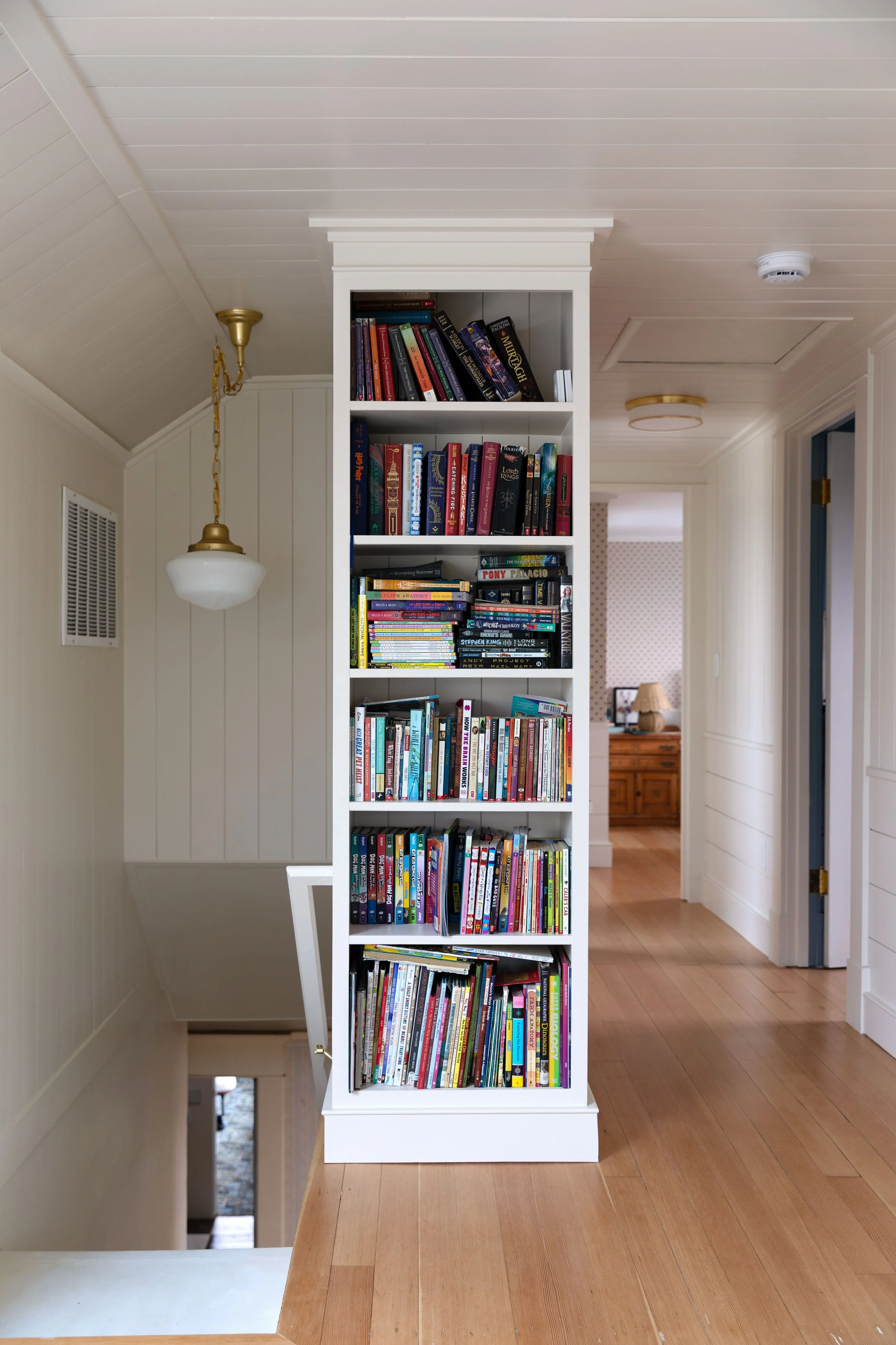 Floor-to-ceiling built-in bookcase serving as a stair guard on an old-house landing