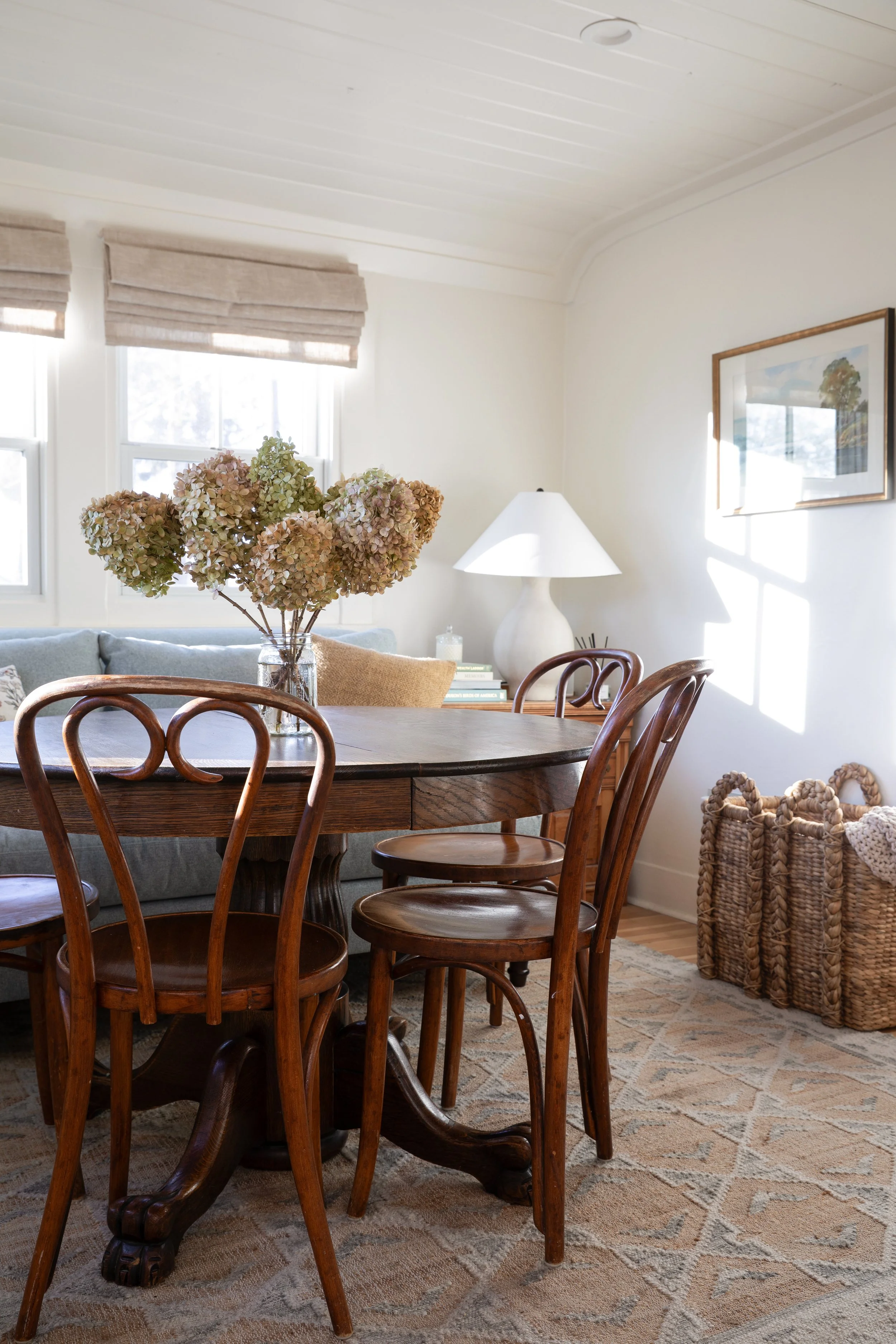 Angled view of the Poplar Cottage sitting and dining room with flatweave rug, vintage table, sofa, and basket for blankets