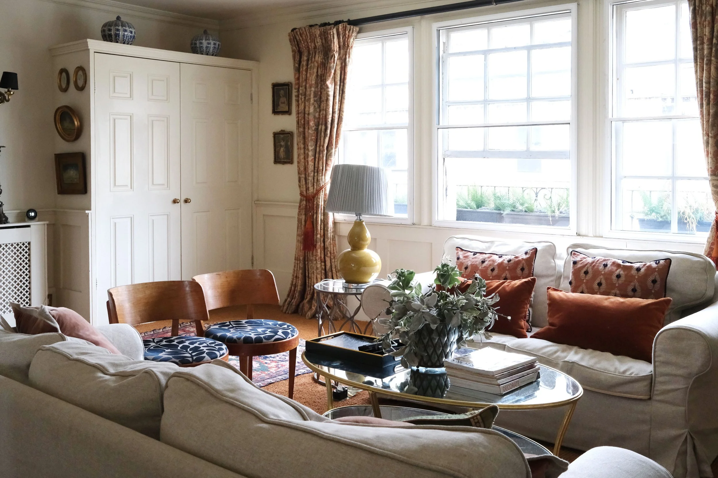 Comfortable white sofa surrounded by vintage paintings, books, brass lighting, and antique furniture