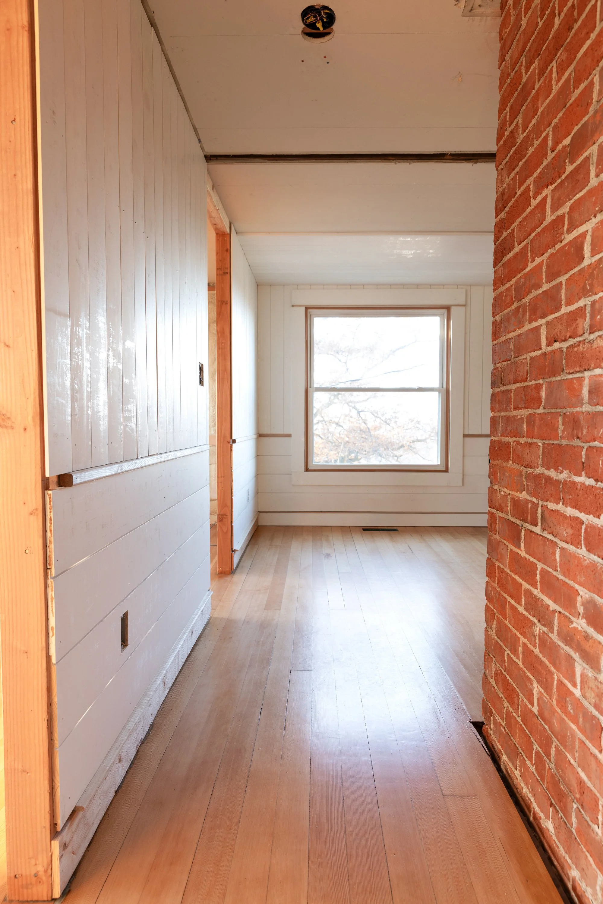 Finished fir floors at the Hill House with exposed brick chimney and paneled walls