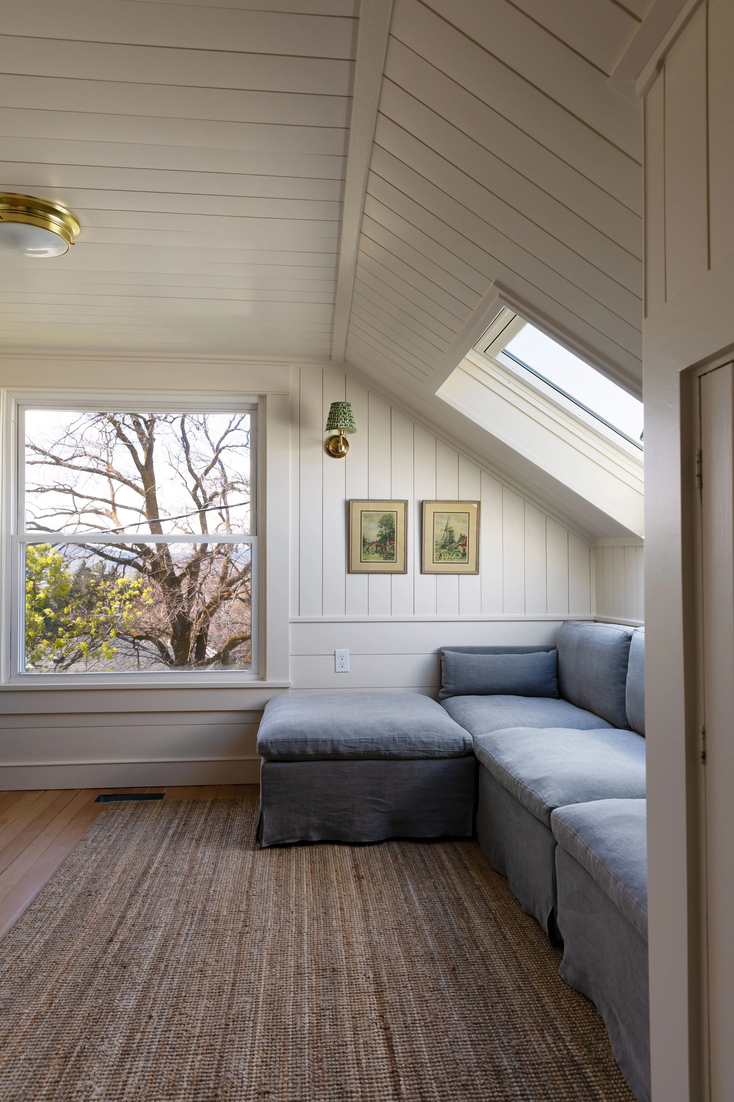 Small upstairs snug with low ceilings, sectional sofa, skylight, and vertical paneling in our Hill House
