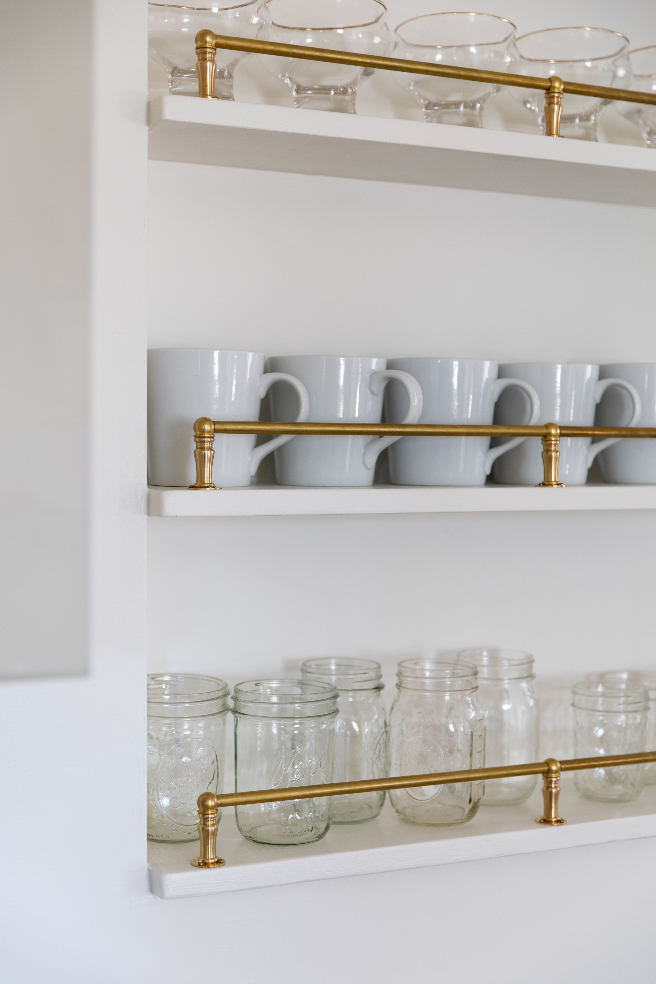 Close-up of brass gallery rail and glassware on recessed shelves.