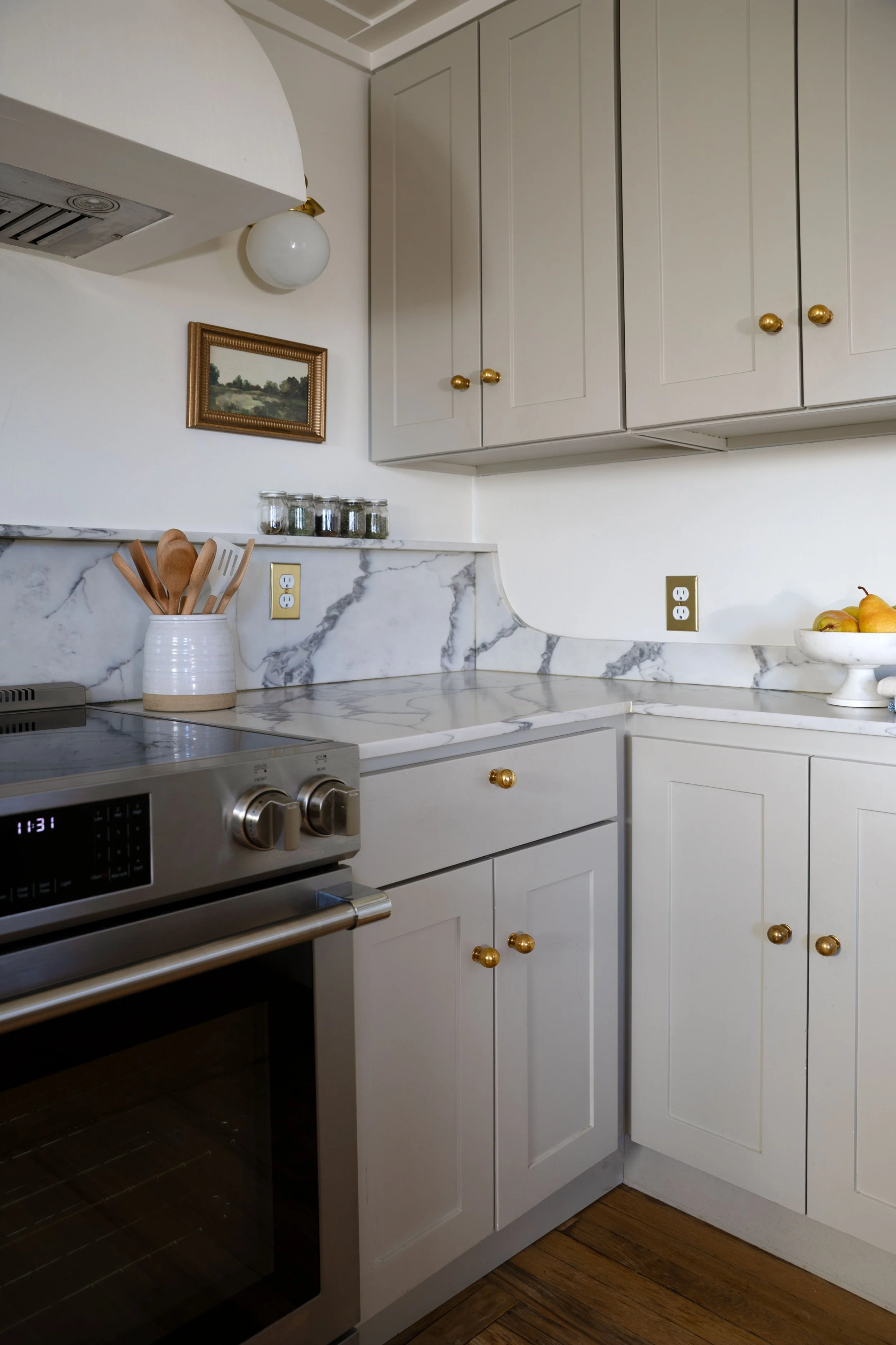 Corner of kitchen with quartz backsplash, curved edge detail, small shelf, and brass hardware.