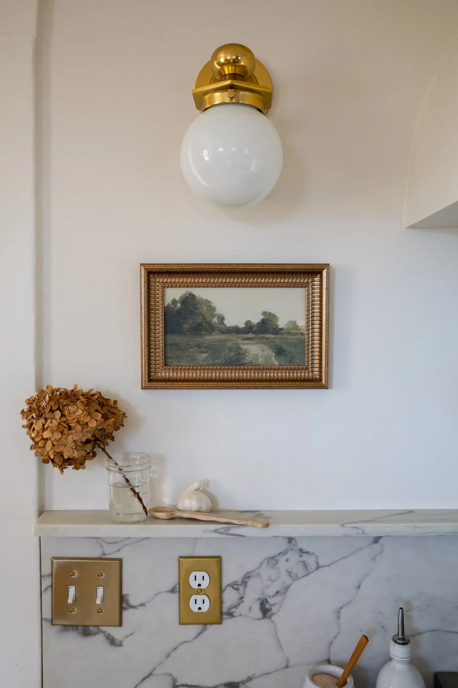 Close-up of vintage-style artwork framed below brass sconce on range wall.