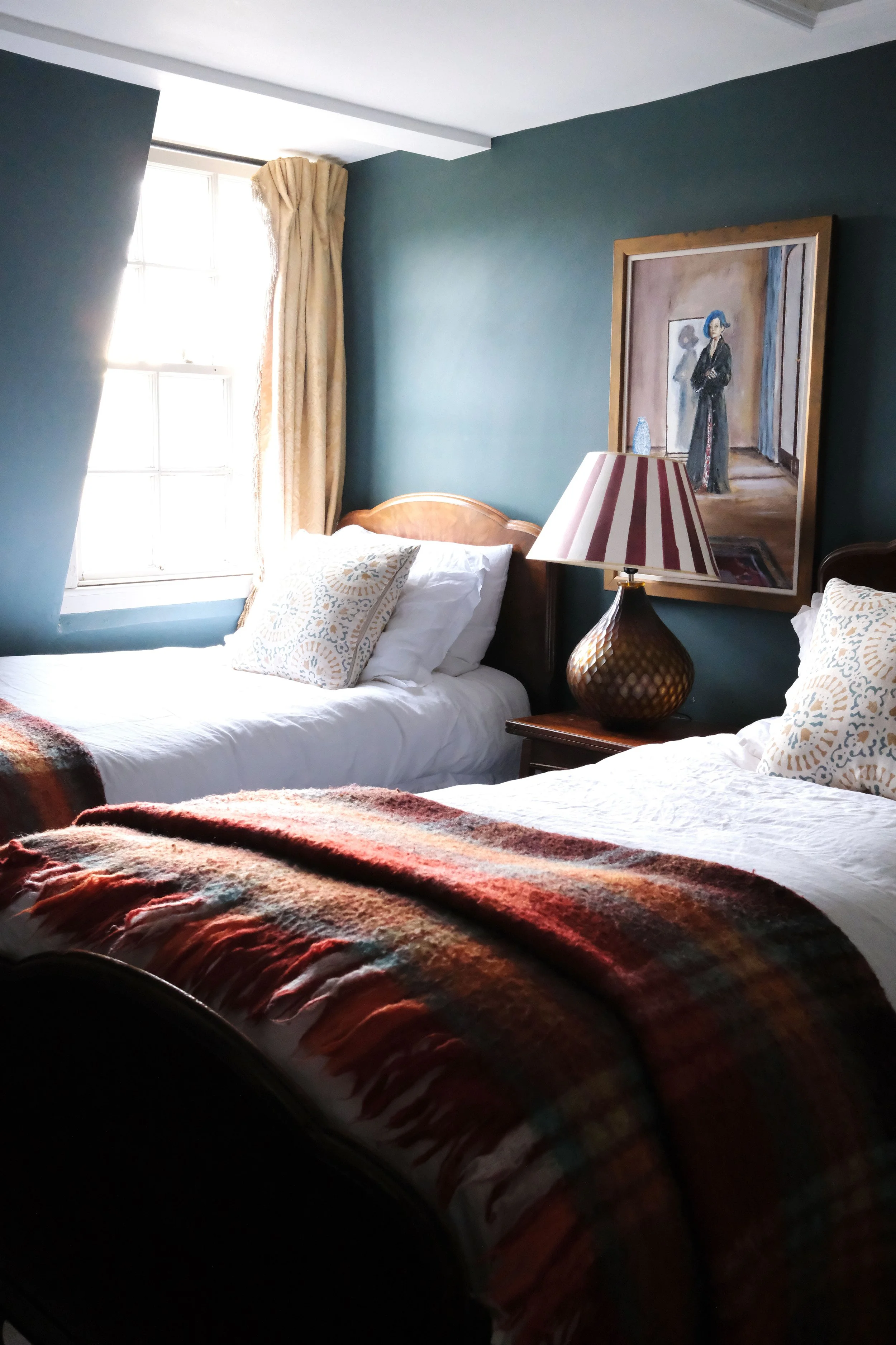Deep blue-green bedroom with twin beds, vintage artwork, and antique furniture