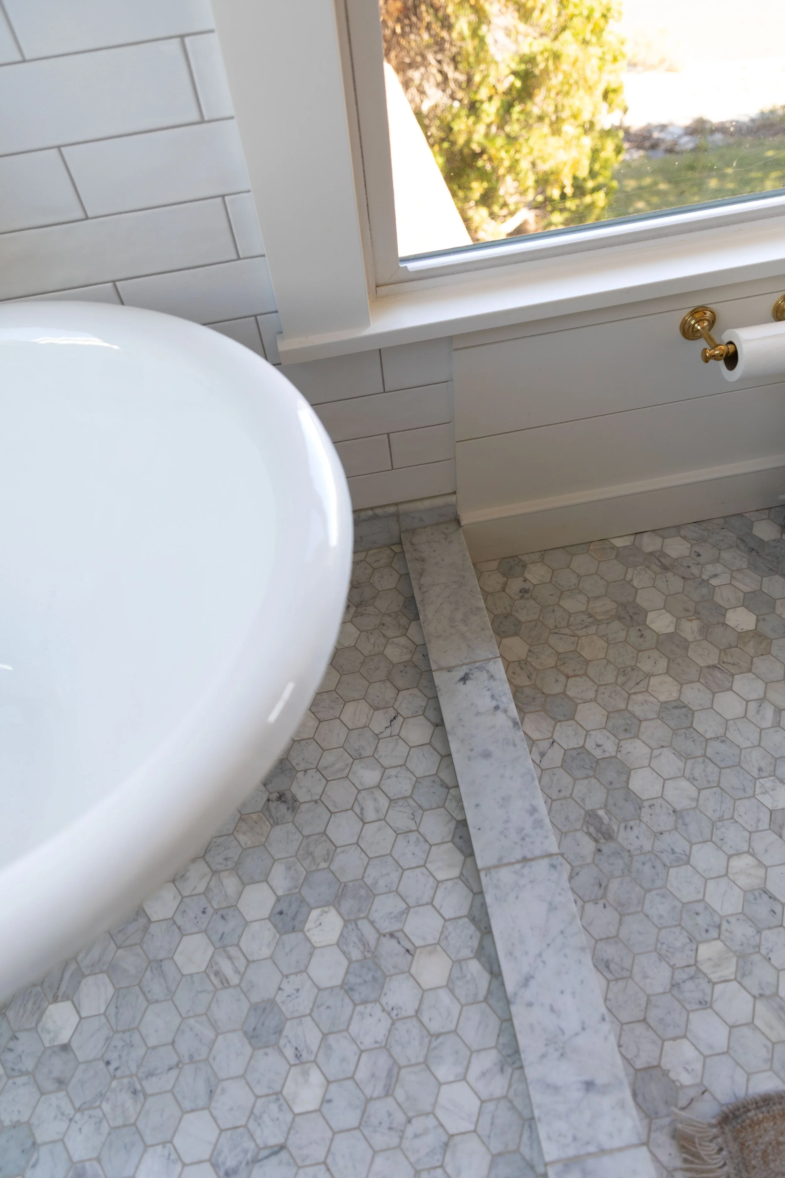 Marble curb strip on a hexagon tile wet room floor beside a clawfoot tub