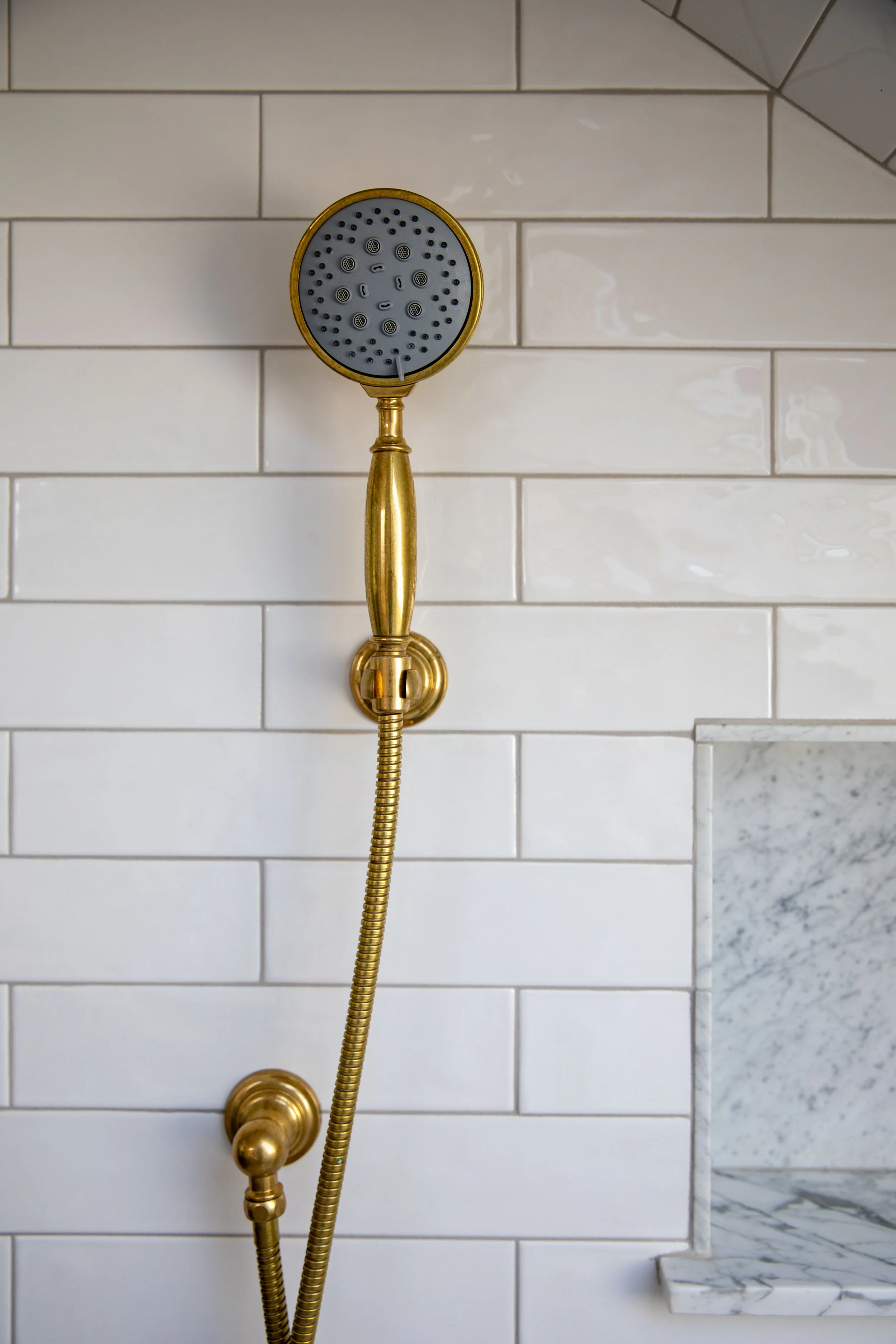 Our uncoated brass handheld shower on white subway tile in the Hill House ensuite bathroom