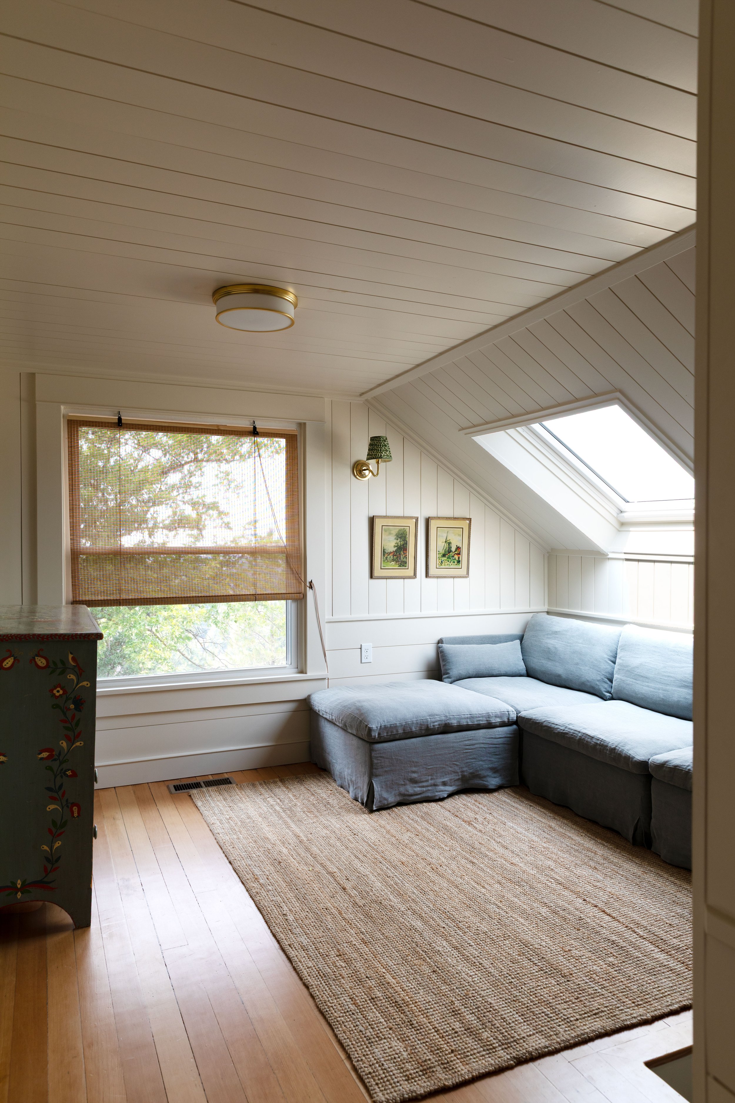 Finished upstairs landing and snug with sectional, skylight, woven shade, and wood floors