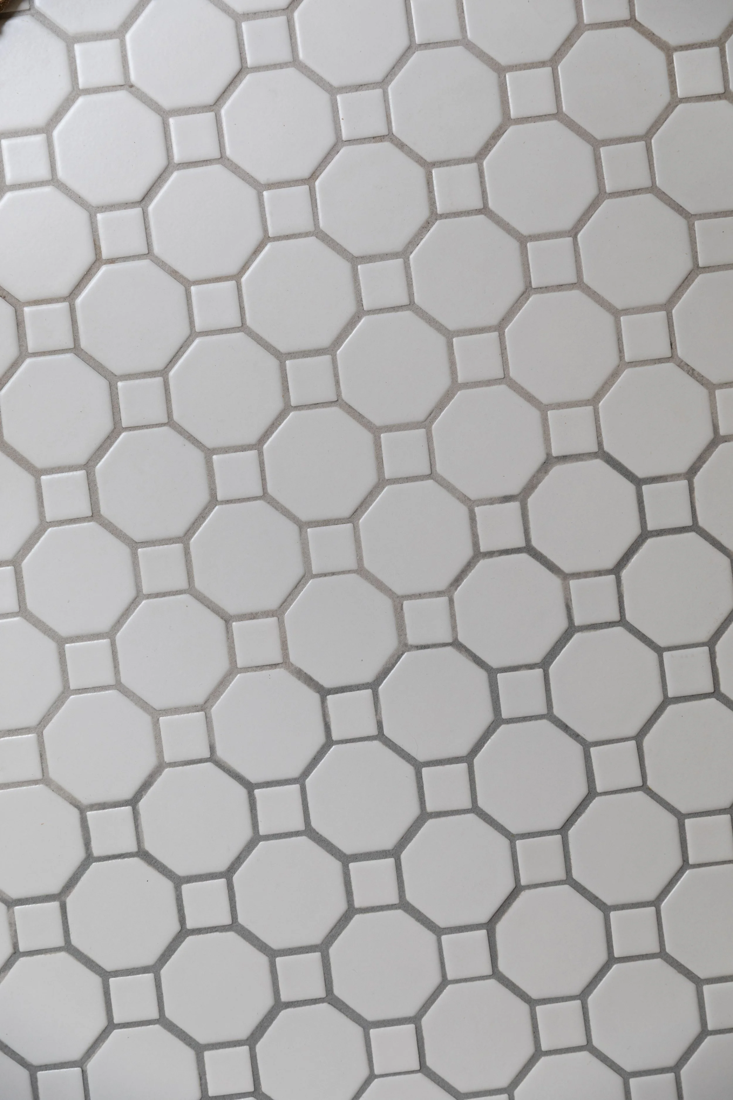Close-up of bathroom floor highlighting dramatic epoxy grout color variation between batches